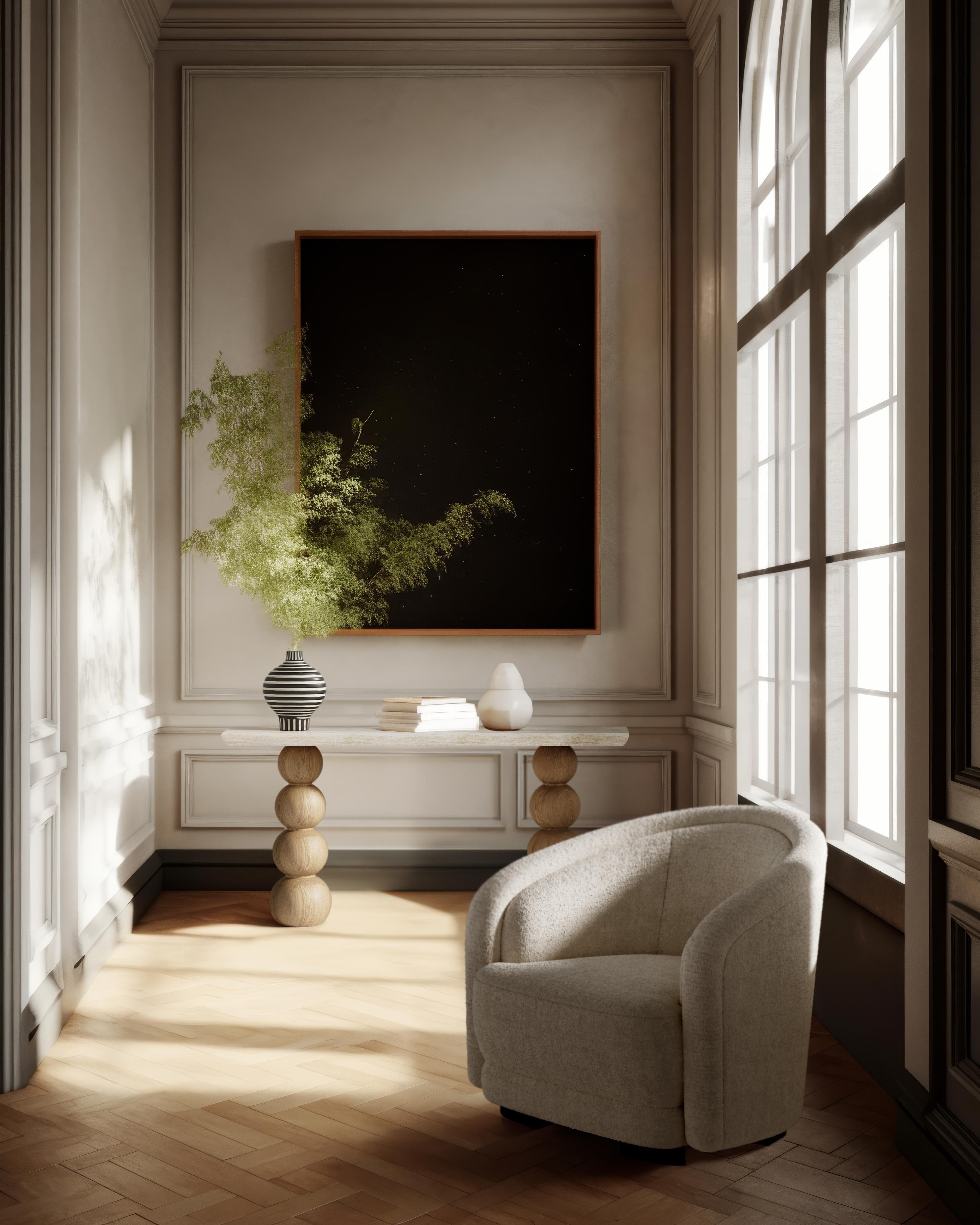 The Chloé console table features a thick travertine top with a curved profile, balanced on two generously proportioned solid Oak hand-turned legs. These legs are reminiscent of the spool-shaped 