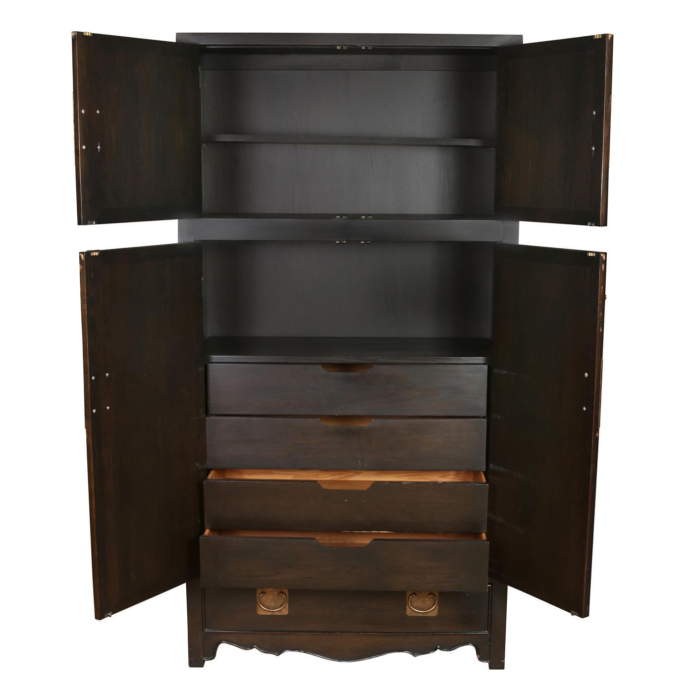 A painted Asian style tall chocolate brown armoire with brass hardware. Two doors open at top with two shelves inside. Two large doors open in the center to reveal four drawers and one large shelf. A single drawer is at the base. Marked John Stuart