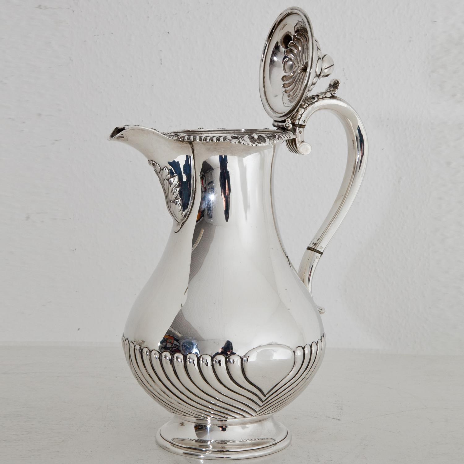 Silver chocolate pot (774g) with a gadrooned belly and ear-shaped handle. The lid and the nozzle are decorated with leaves, the node is in the shape of a cocoa pod. At the bottom, lid and handle are the hallmark of E.J. & W. Barnard.