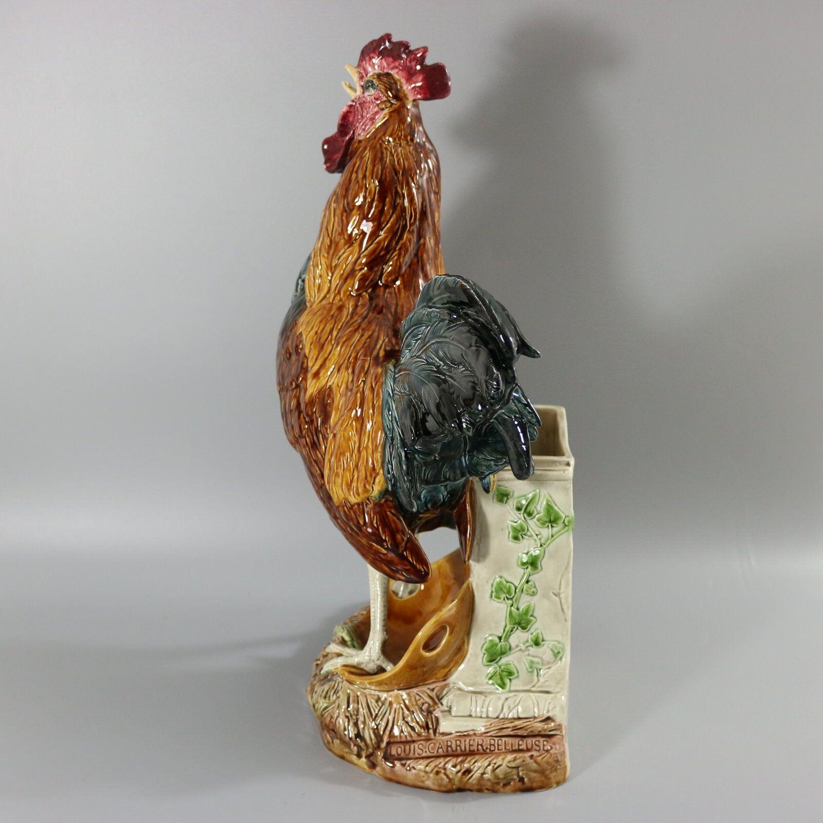 Choisy Majolica figural vase which features an animated cockerel / rooster stood on a basket, in front of a stone wall. Ivy grows up the wall. Colouration: light brown, brown, blue/grey, are predominant. The piece bears maker's marks for the Choisy
