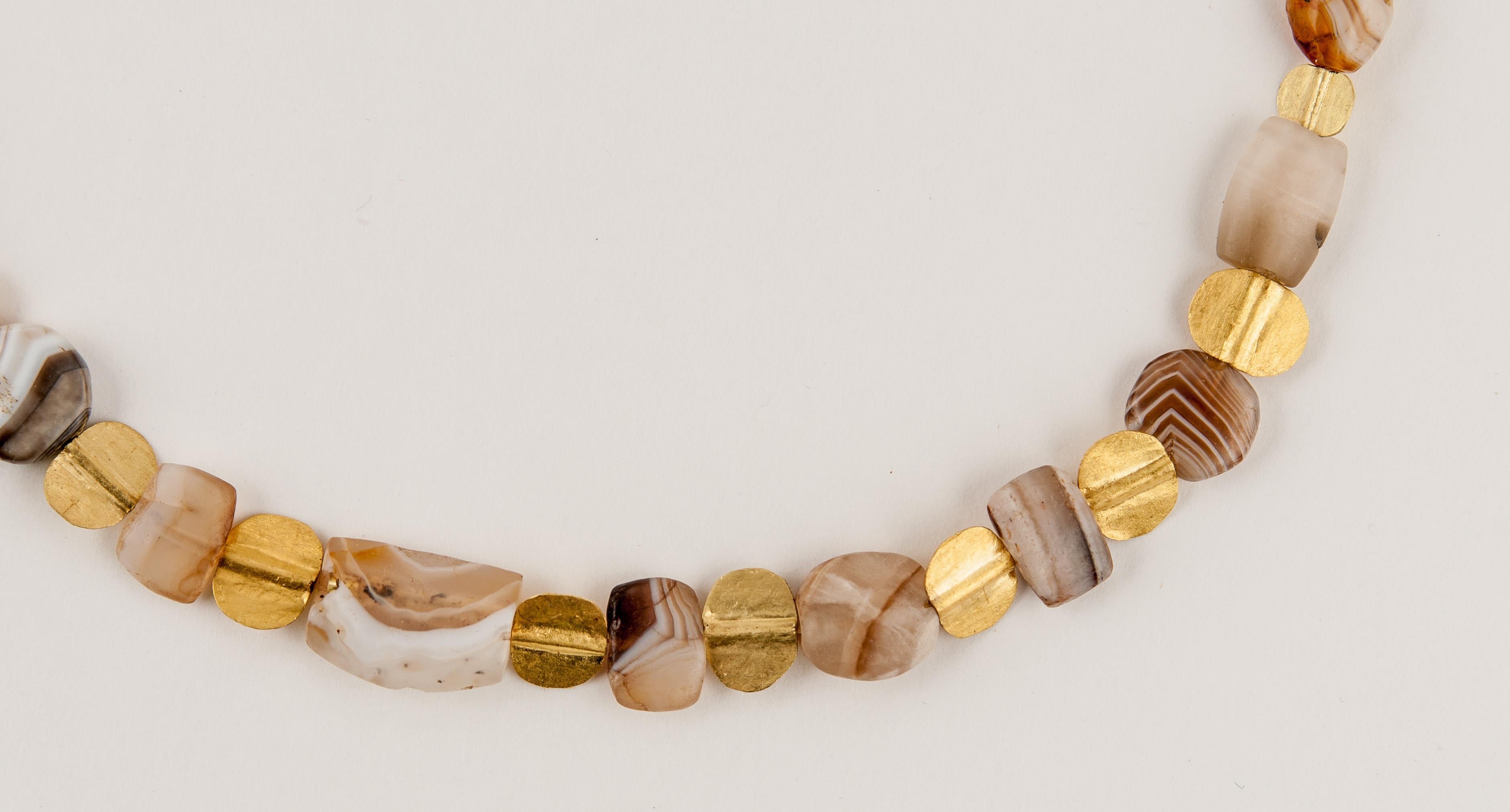 Twenty-three tabular agate beads, agate beads of trapezoidal shape, rectangular shape, ovals and circles and a bow bead in the center, alternating with twenty-two tabular 20k gold beads. The tabular gold beads graduate in size from the front of the