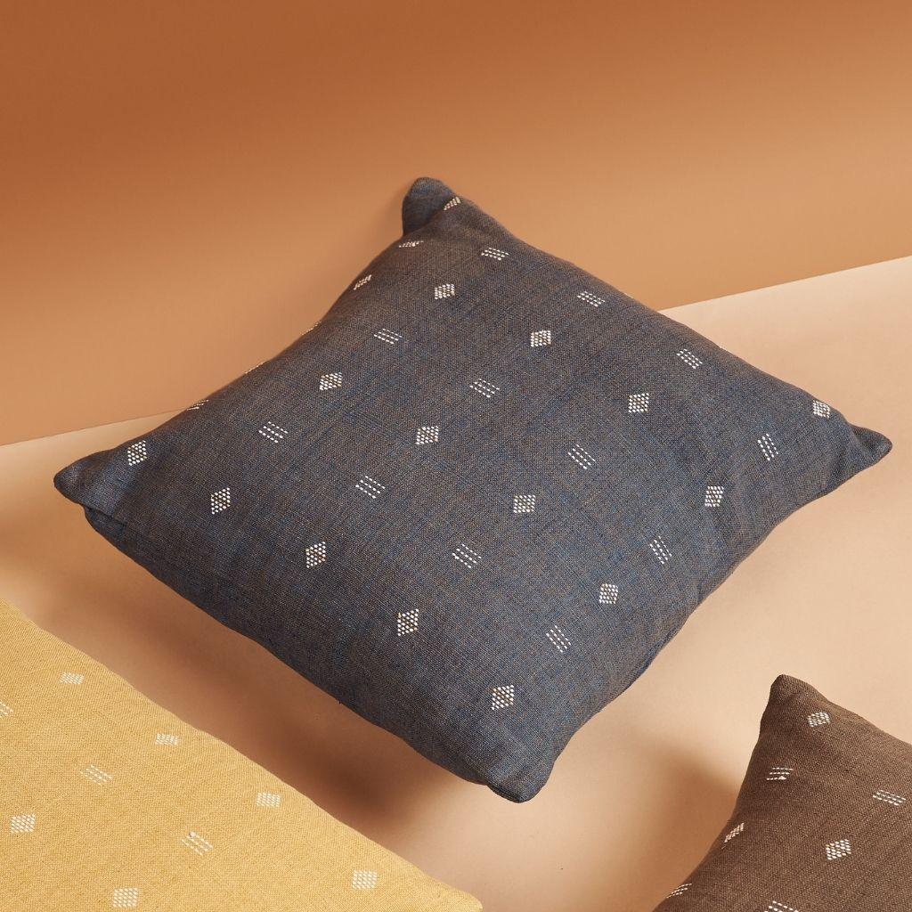 Nira Indigo Pillow is a slightly textured handwoven pillow where our artisans have skillfully created a classic pattern using an ancient weaving technique. Undyed yarn is used as a design element with the backdrop of pleasant hues of dusted indigo.