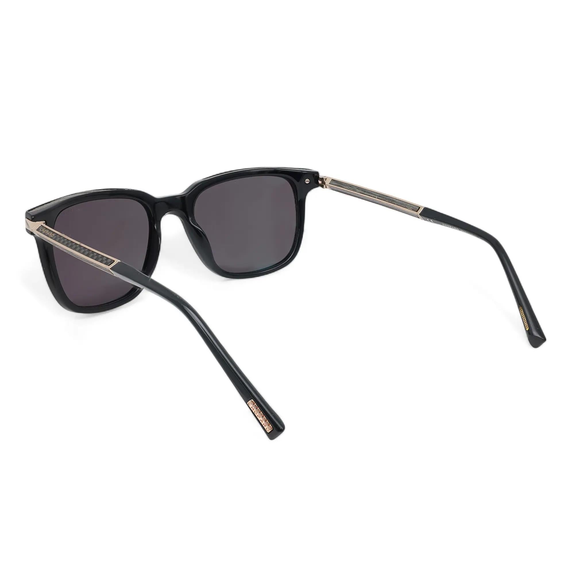 Introducing the luxury unisex Chopard Sunglasses 95221-0521, perfect for street fashion. These sunglasses showcase a shiny black with wood and carbon fiber metal acetate frame with smoke polarized lenses. The arms are elegantly adorned with the