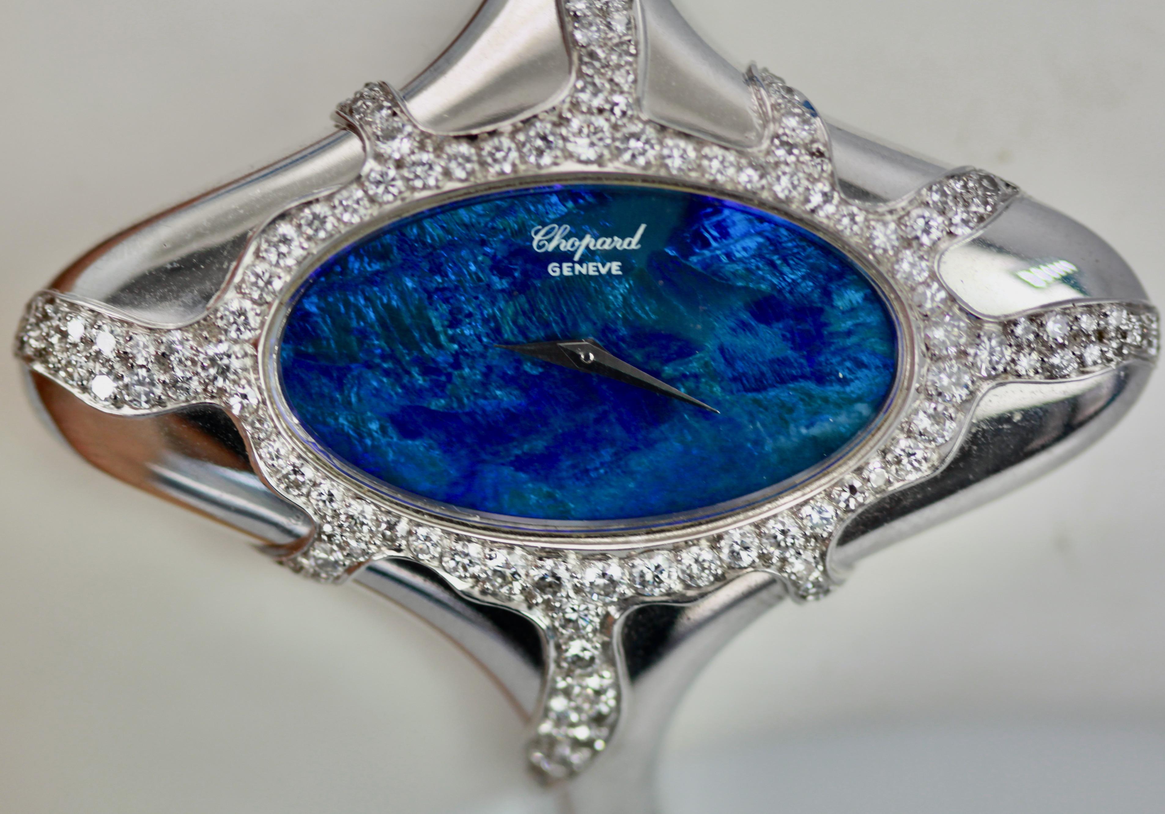 This Chopard Opal Diamond Watch is done in 18K white gold, Black Opal Face, manual wind Ladies Wristwatch.  The Opal measures 3 cm x 2 cm and is covered in Diamonds.  There are Diamonds around the face of the watch and down the sides in a starburst