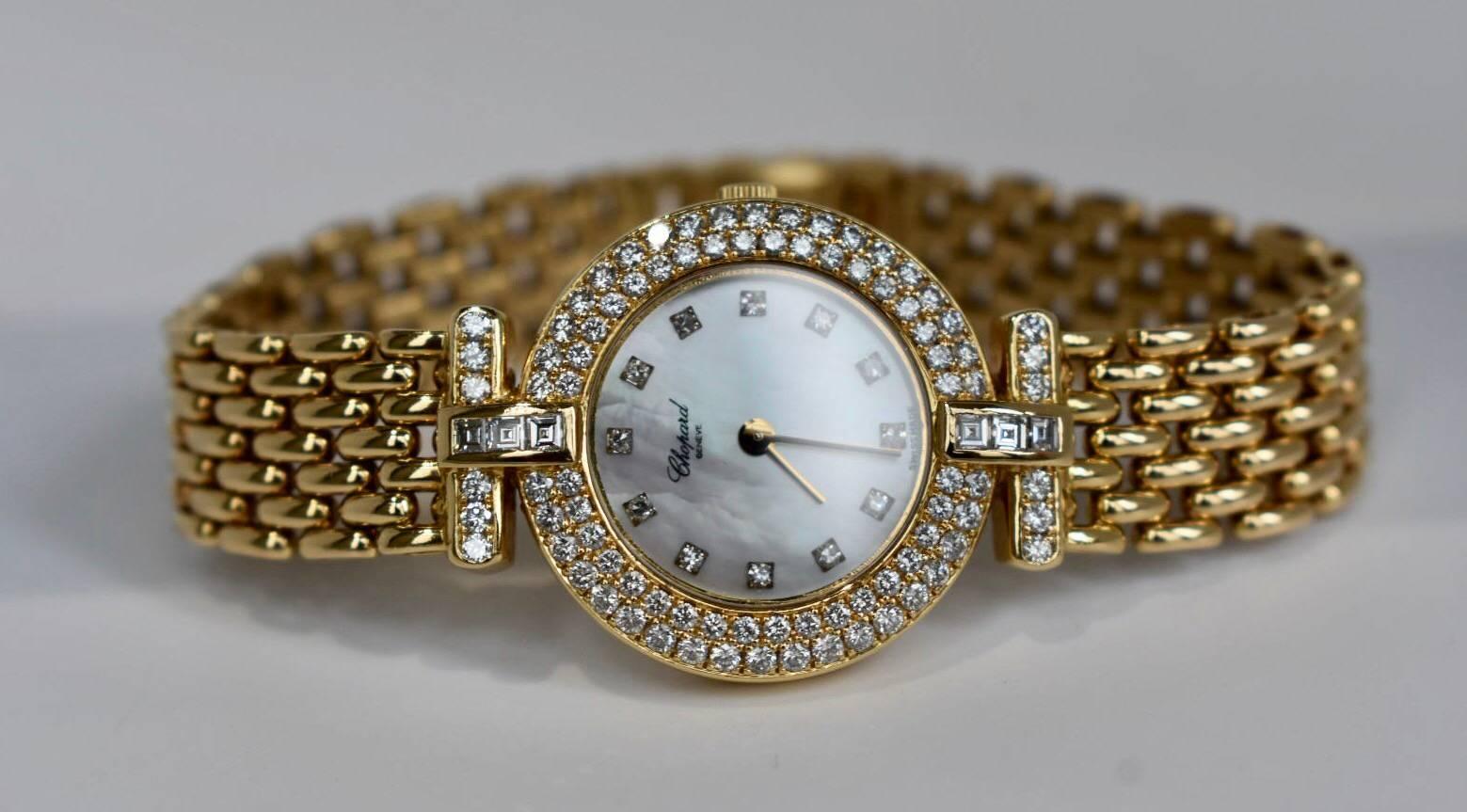 A Chopard diamond watch set in 18k yellow gold. The watch features a mother of pearl dial with diamond markers and diamond bezel. The band has addition diamonds and three square-cut diamonds on either sides of the strap.
The watch is sold with the