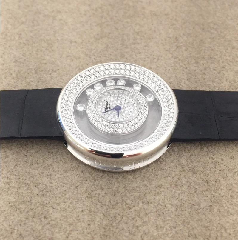 Chopard Happy Diamonds in 18k White Gold case set with diamonds and a clear panel housing seven floating diamonds. The diamond studded dial features no markers and just two hands. The dazzling case is held by leather straps and fastened with a
