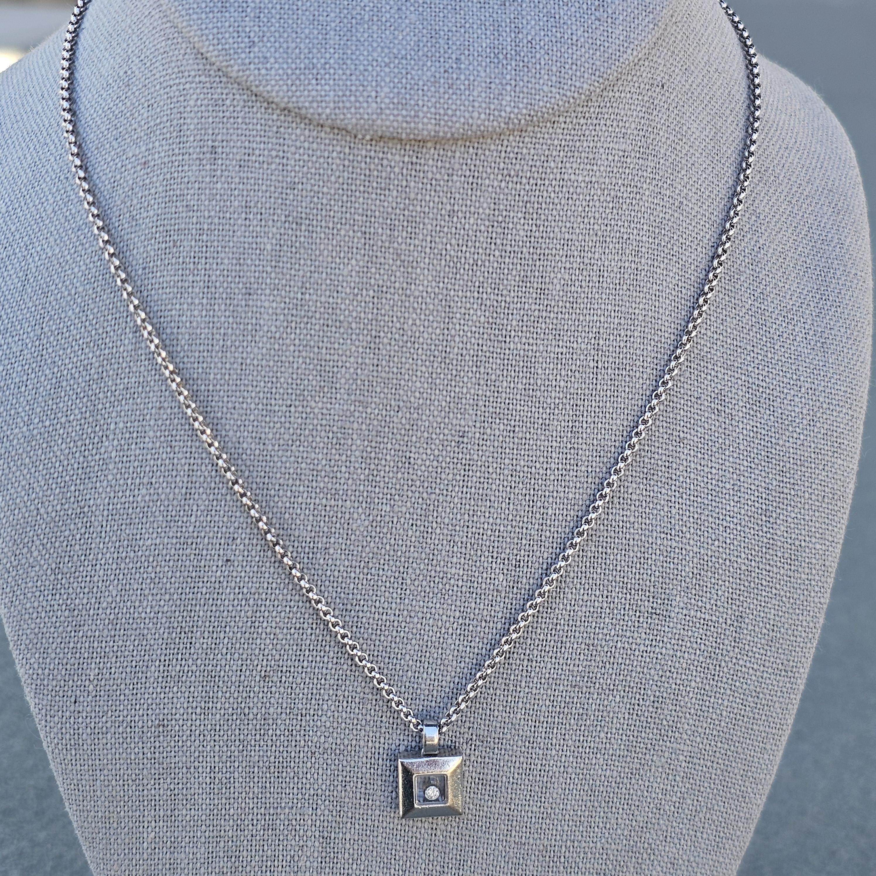Nous avons ici un superbe collier pendentif carré flottant Happy diamond de Chopard, orné d'un diamant blanc rond serti dans de l'or blanc 18k.

Plus d'informations :
Dimensions : chaîne de 16,5