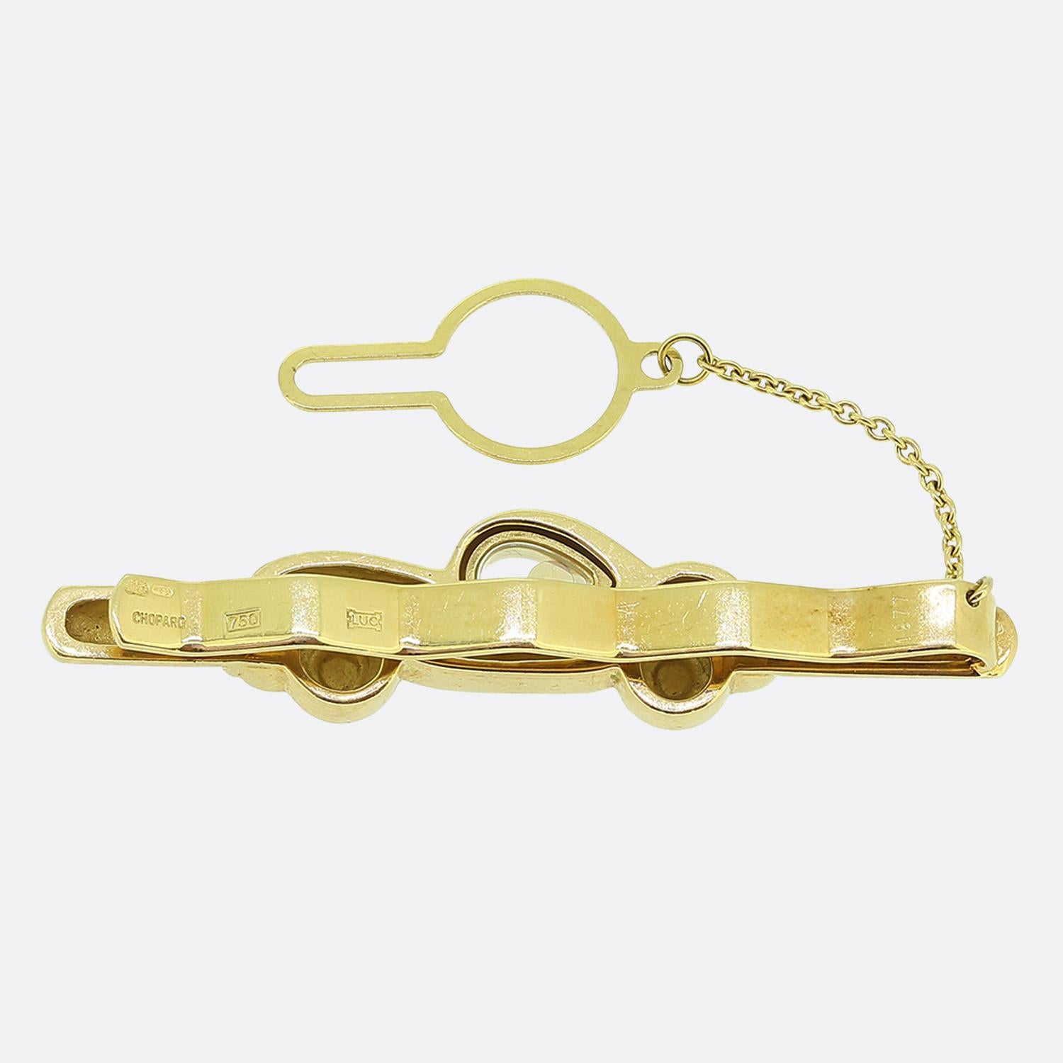 Voici une pince à cravate originale créée par le célèbre joaillier français Chopard. Réalisé en or jaune 18 carats, ce modèle présente un motif de voiture élégante, avec des roues détaillées et une carrosserie aérodynamique. Au cœur de la voiture,