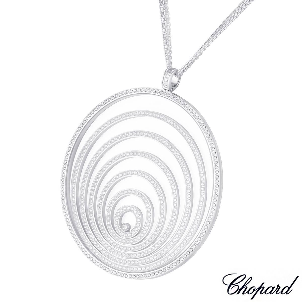 An 18k white gold diamond set pendant from the Happy Spirit collection by Chopard. The pendant features a large circular disk containing 6 floating rings graduating in size behind the Chopard signed glass, with a single floating diamond enclosed