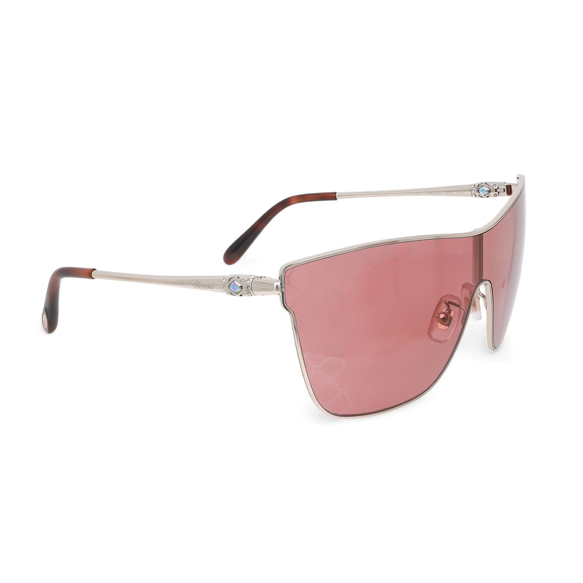 Introducing the luxury unisex Chopard Sunglasses 95221-0406, perfect for street fashion. These sunglasses showcase a shiny light gold metal frame with orange with logomania mirrored lenses. The arms are elegantly adorned with the Chopard logo. The