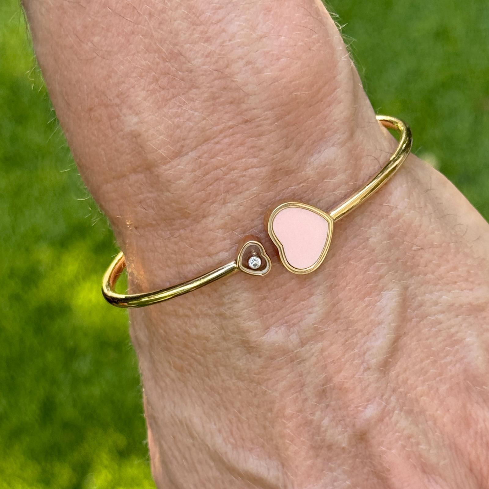 Playful elegance meets timeless design in this Chopard Happy Hearts bangle, crafted in 18 karat rose gold. One end features a heart-shaped rose stone, while the other showcases a signature floating diamond encased in a transparent heart-shaped