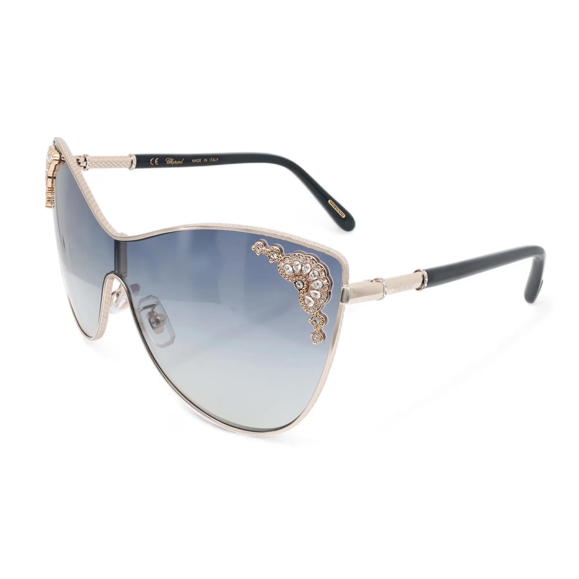 Presenting the luxury unisex Chopard Sunglasses 95221-0446, ideal for street fashion. These sunglasses feature a shiny rose gold metal/acetate frame with strass and smoke gradient lenses. The arms are adorned with the Chopard logo. The dimensions