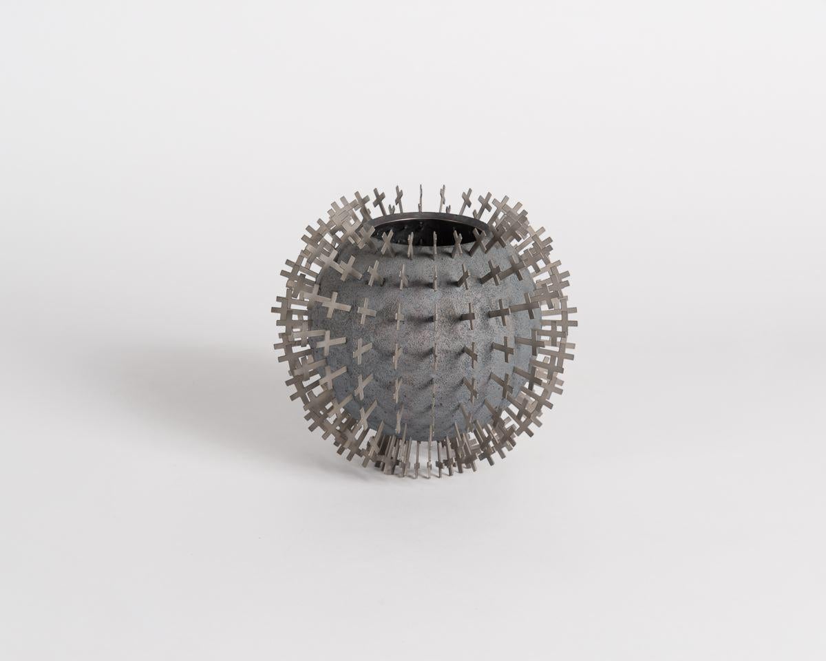 Il lavoro di Chris Knight si colloca ai confini tra arte, artigianato e design. Questa ciotola scultorea in argento e acciaio inossidabile è ricoperta da decine di croci ben posizionate, tutte allineate come se emergessero dal centro della sfera.