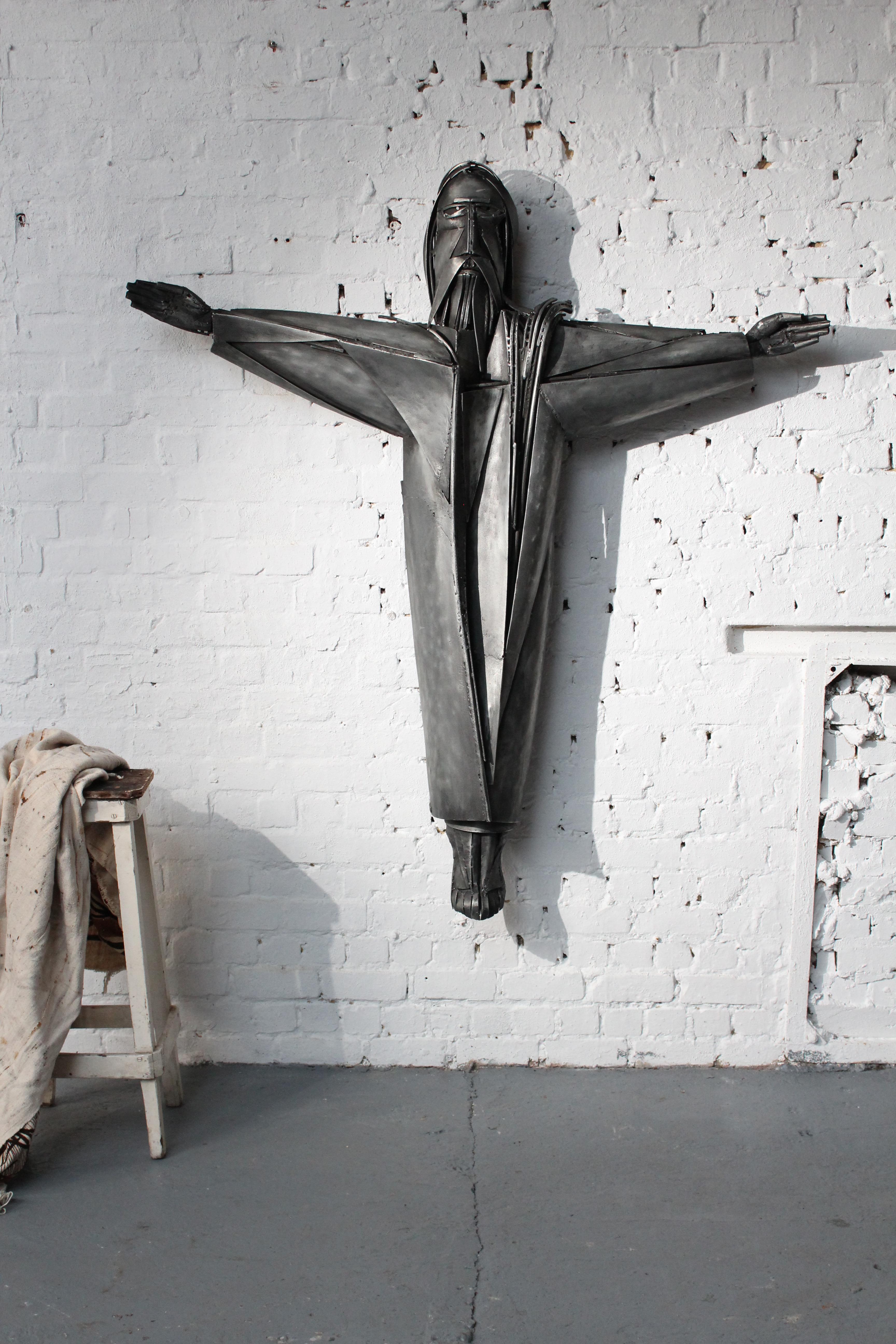 Cristo (altezza 160 cm) dello scultore belga Roger Bonduel (1930-2019) in acciaio saldato e patinato. Dal 1961 al 1966, Roger Bonduel ha insegnato arte visiva all'Academy Arts di Bruges. Bonduel divenne famosa soprattutto per le sue sculture, i suoi
