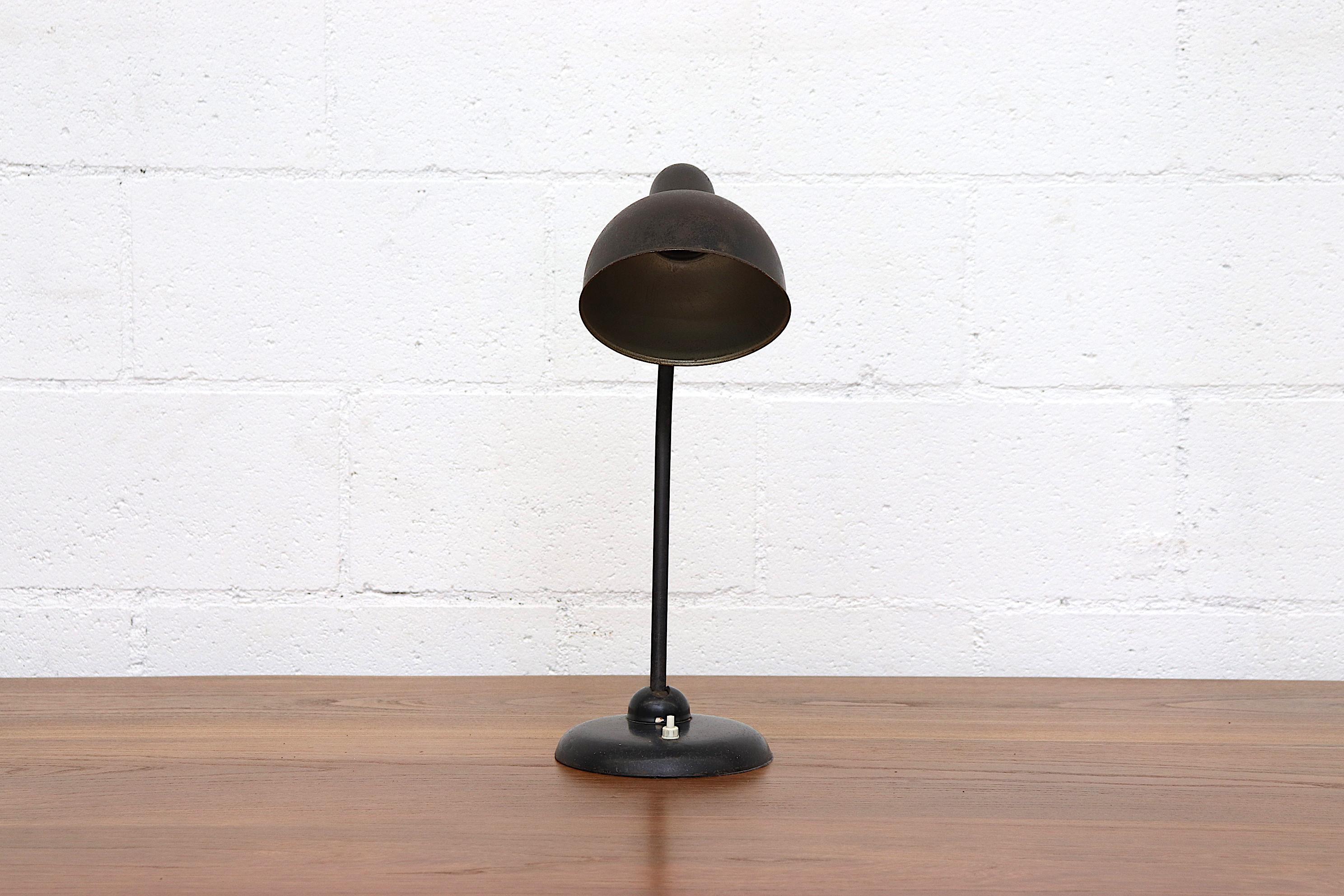 Black enameled Kaiser Idell table lamp with swivel joint and original production stamp. Well patinaed with tilting arm and white acrylic light switch. CE marked and in original condition with visible wear and minimal surface rust consistent with age.
