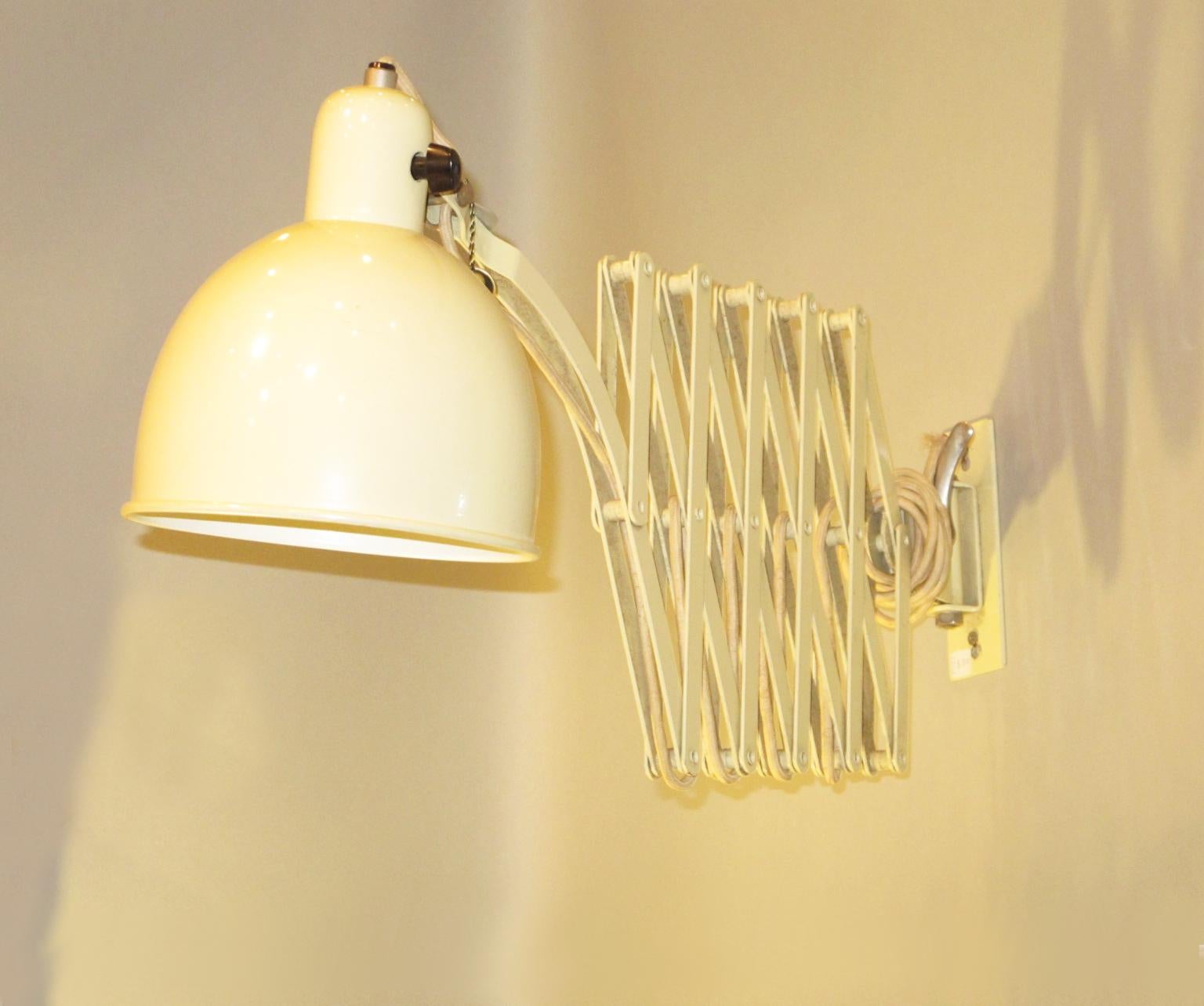 This is an original extendable metal wall lamp, scissor sconce, designed by famous Bauhaus school metal workshop foreman Christian Dell in 1933 for Kaiser Idell. This large version has an off-white enameled paint metal and chromed screws. The lamp