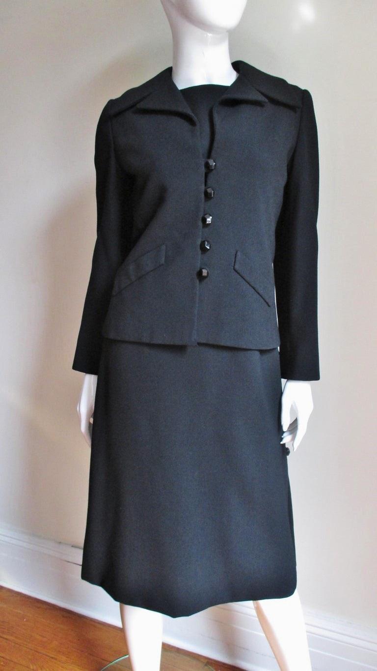 A rare 2 piece black wool dress and jacket set from the early collections of Christian Dior designed by the master himself.  The dress is sleeveless with a crew neckline, a seam below the bust and 6 decorative black glass faceted buttons and loops