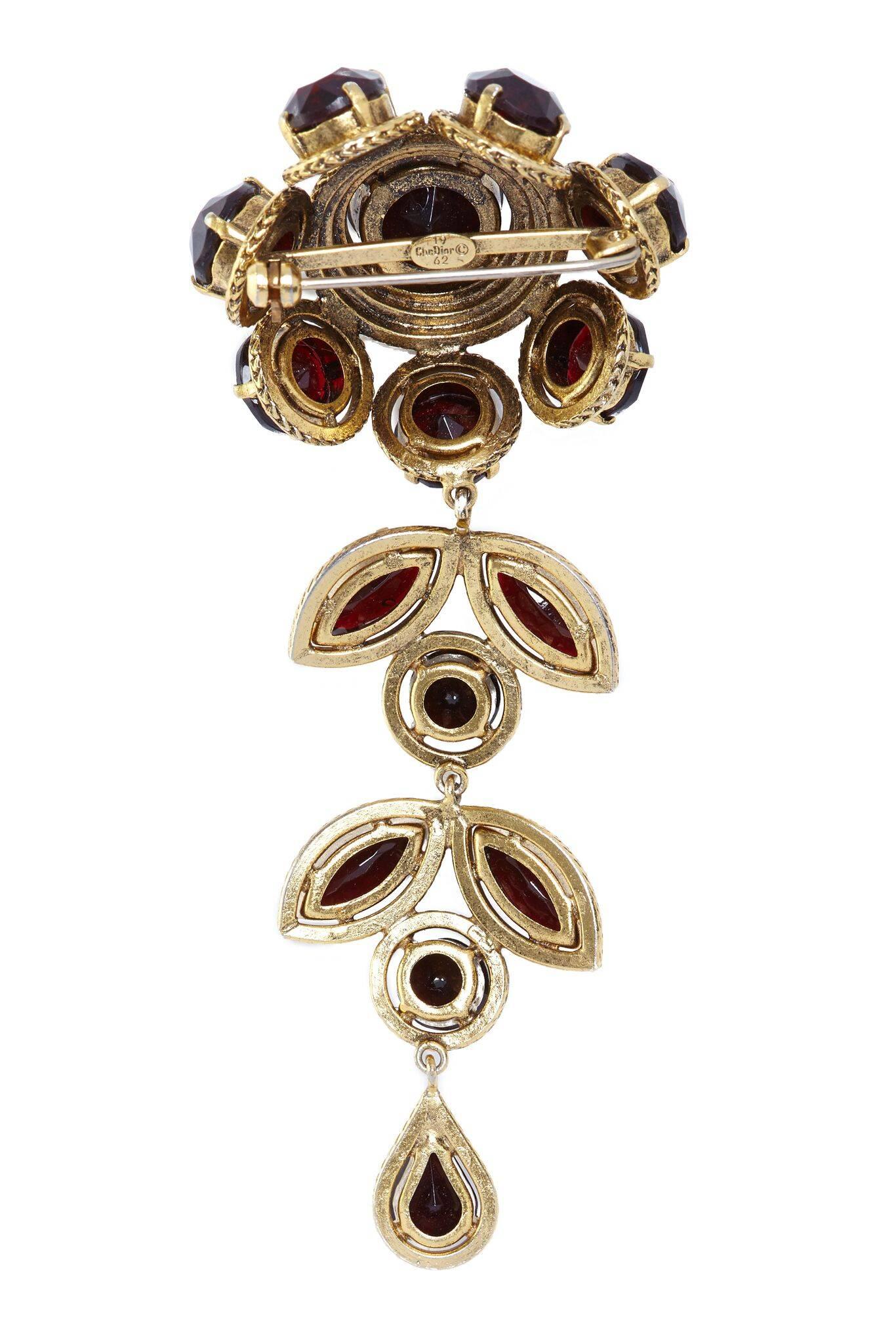 This magnificent 1960s Christian Dior flower drop brooch with prong set rhinestones is in superb vintage condition. Large cut glass rounds in rich garnet red are arranged into a large gold gilt floral design with a lengthly drop detail. The drop is