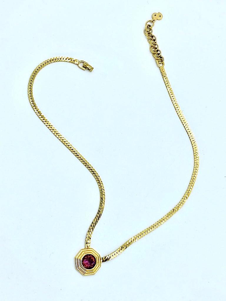 A charming Christian Dior necklace from the 1970s in gold plate with purple rhinestone pendant. The pendant is a stepped octagon shape .69 of an inch wide and tall and set with a .38 of an inch diameter purple rhinestone. The flat herringbone style
