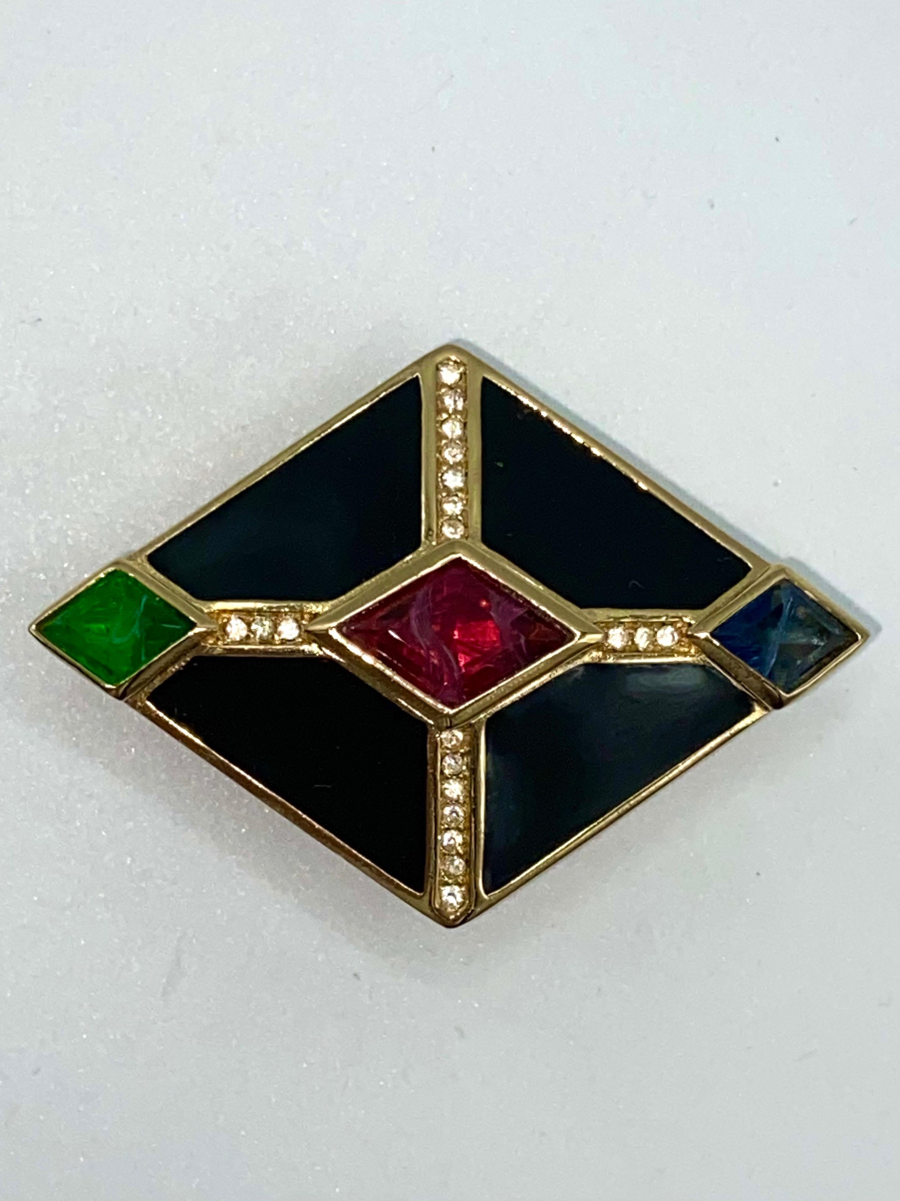 An elegant 1980s Art Deco style brooch by Christian Dior. The diamond shape brooch has black enamel on gold and is set with three diamond shape glass stones. The faux emerald, ruby and sapphire stones show steaks of white in them in same manner as