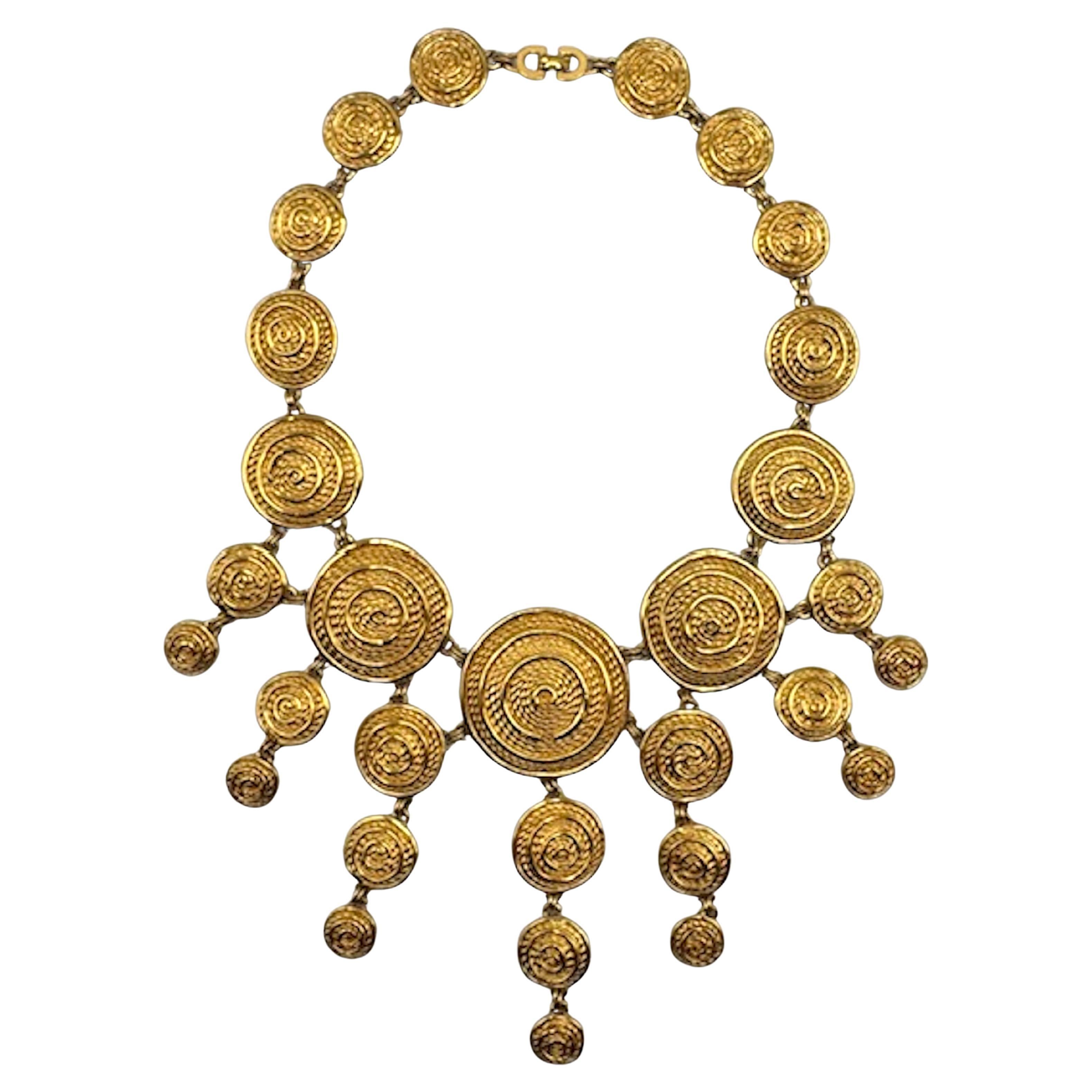 This vintage 1980s Christian Dior necklace is a bold statement piece crafted in rich gold-tone plate featuring a bib of numerous disks with a nod to ancient Etruscan design. The necklace is composed of a series of concentric, textured spiral discs