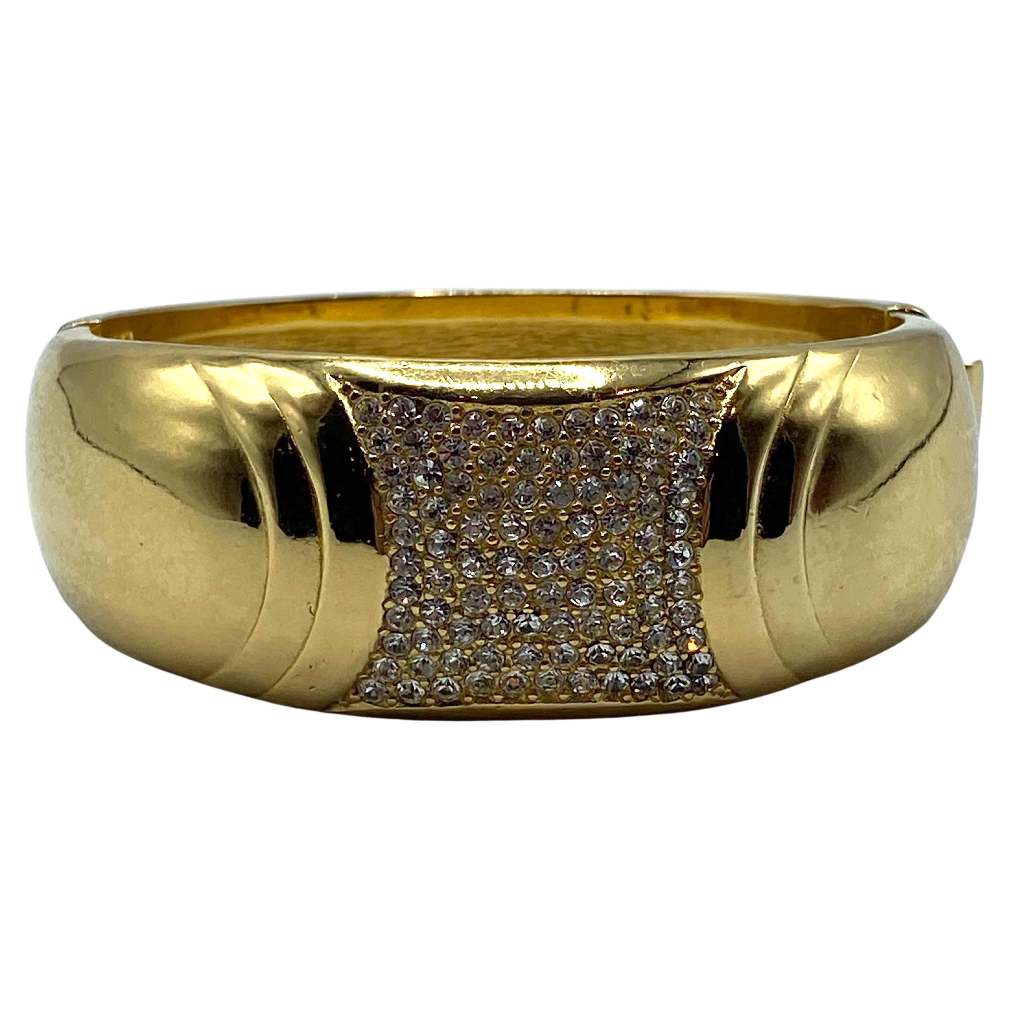Elegant in its simplicity of design with a subtle nod to the Art Deco is this Christian Dior bracelet from the 1980s The top is accented with a 1 inch center of pave' rhinestones. The polished shiny gold plated bangle is .94 of an inch wide at the