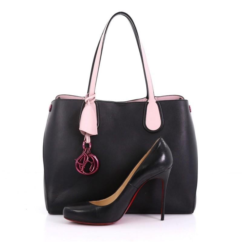 This Christian Dior Addict Shopping Tote Leather Small, crafted in black leather, features dual slim pink leather handles, side snap buttons, Dior charms and pink-tone hardware. Its magnetic snap closure opens to a pink leather interior . **Note: