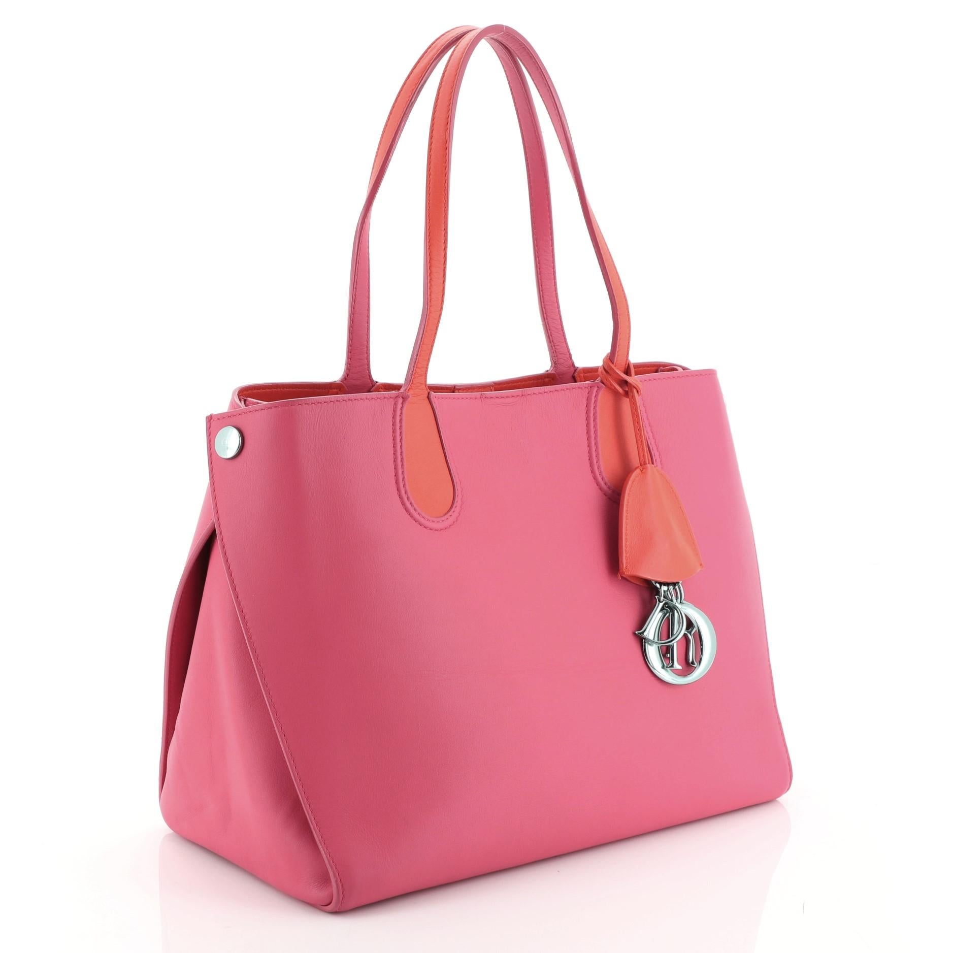 This Christian Dior Addict Shopping Tote Leather Small, crafted in pink leather, features dual slim leather handles, side snap buttons, Dior charms and gunmetal-tone hardware. Its magnetic snap closure opens to an orange leather interior .