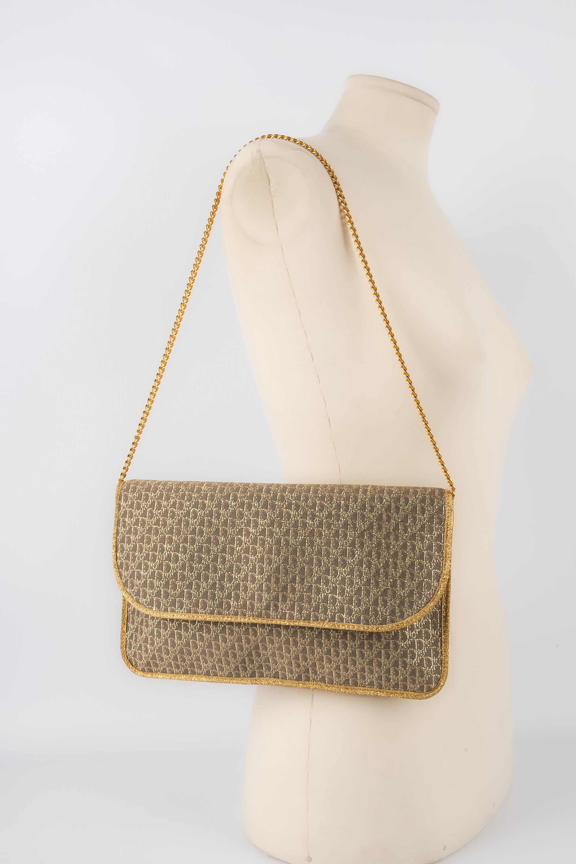DIOR - (Made in France) Golden monogrammed canvas clutch with golden chain handle.

Condition:
Decent condition

Dimensions:
Length: 25 cm - Height: 16 cm - Depth: 1 cm - Handle length: 45 cm

S201
