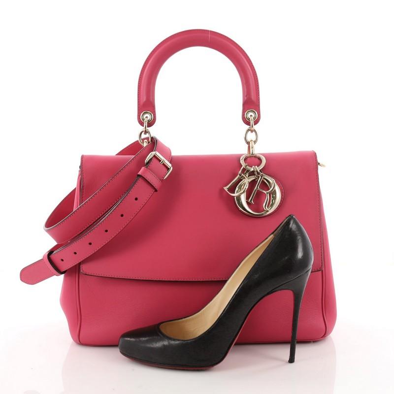 This authentic Christian Dior Be Dior Bag Smooth Leather Small is both bold and beautiful, perfect for every fashionista. Crafted from pink leather, this boxy bag features a leather top handle, sleek Dior charms, side snap buttons, exterior back