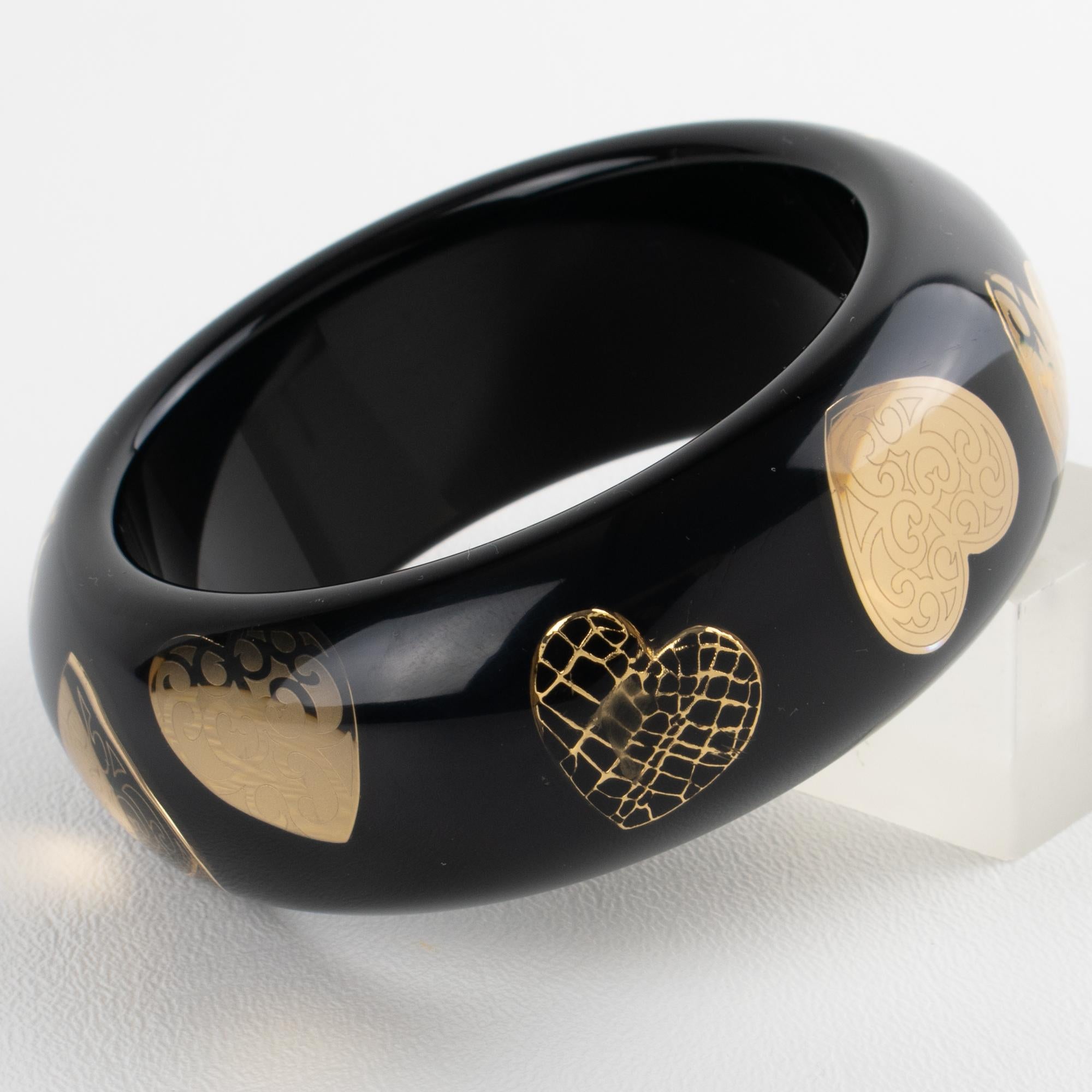 Ce superbe bracelet Christian Dior est composé d'un solide bracelet en acrylique noir ou en Lucite, dans lequel sont incrustés des motifs de cœurs dorés. Le bracelet est gravé sur la tranche du logo emblématique de Dior. Le bracelet est livré dans