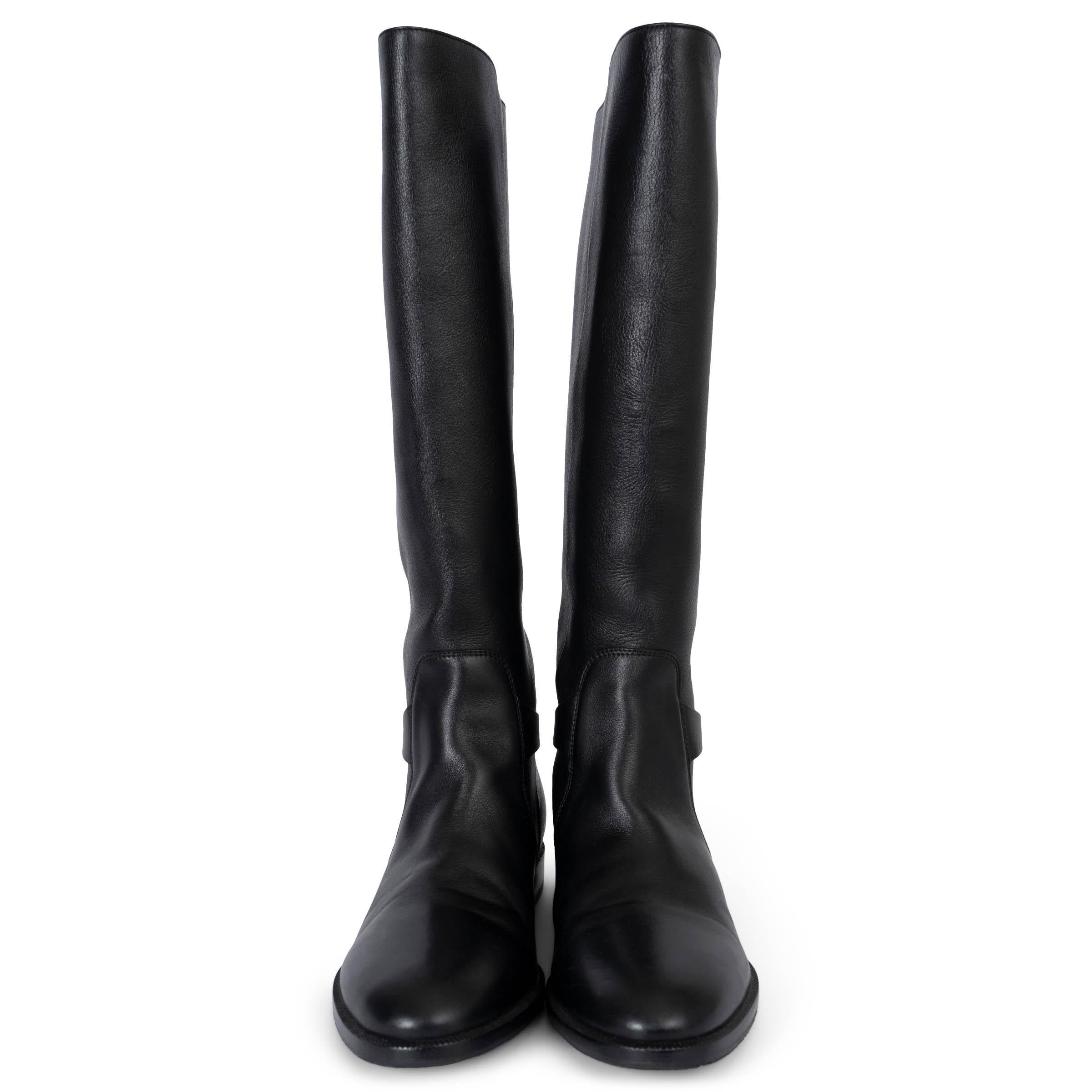 These 100% authentic Christian Dior Empreinte riding boots are crafted from black soft calfskin leather. Featuring a knee-high, pull-on style, they are adorned with a CD buckle and strap at the ankle for a refined touch. The design is completed with