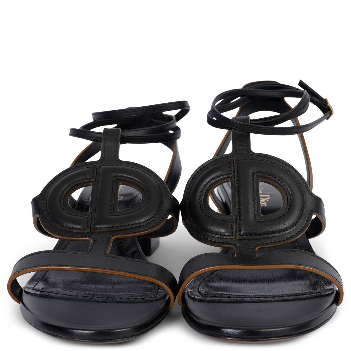 100% authentic Christian Dior D-Club block-heel black leather finished with a camel colored edge. The thin strap wraps around the ankle and closes with a gold colored buckle. On the front of the sandal you can find the big but discrete CD logo.