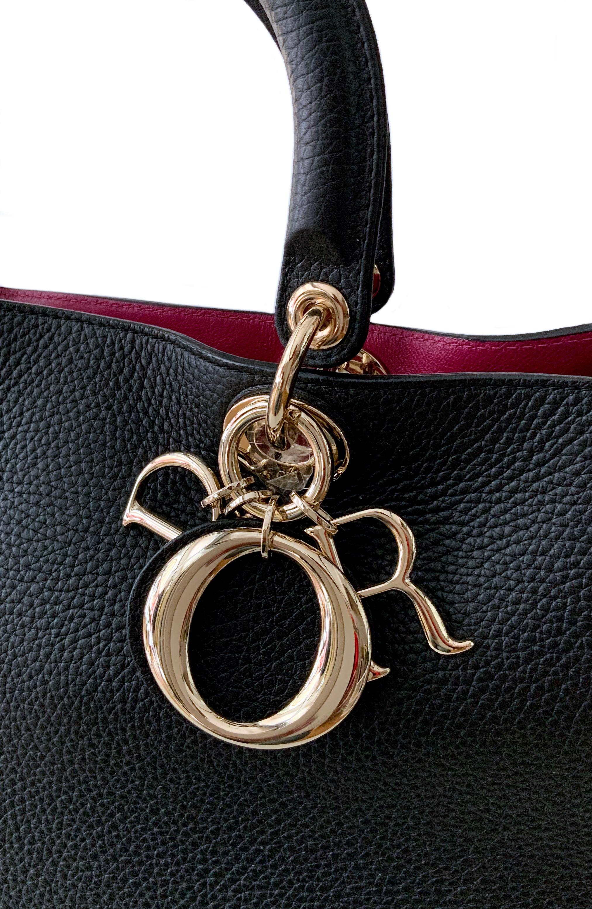 Die ikonische:: gebrauchte:: aber neue Diorissimo Tote Bag aus dem Hause Christian Dior ist aus wunderschönem schwarzem Bullcalf-Leder gefertigt und öffnet sich zu einem Innenraum aus rosa Kalbsleder. 
Sie kann mit einem verstellbaren Schulterriemen