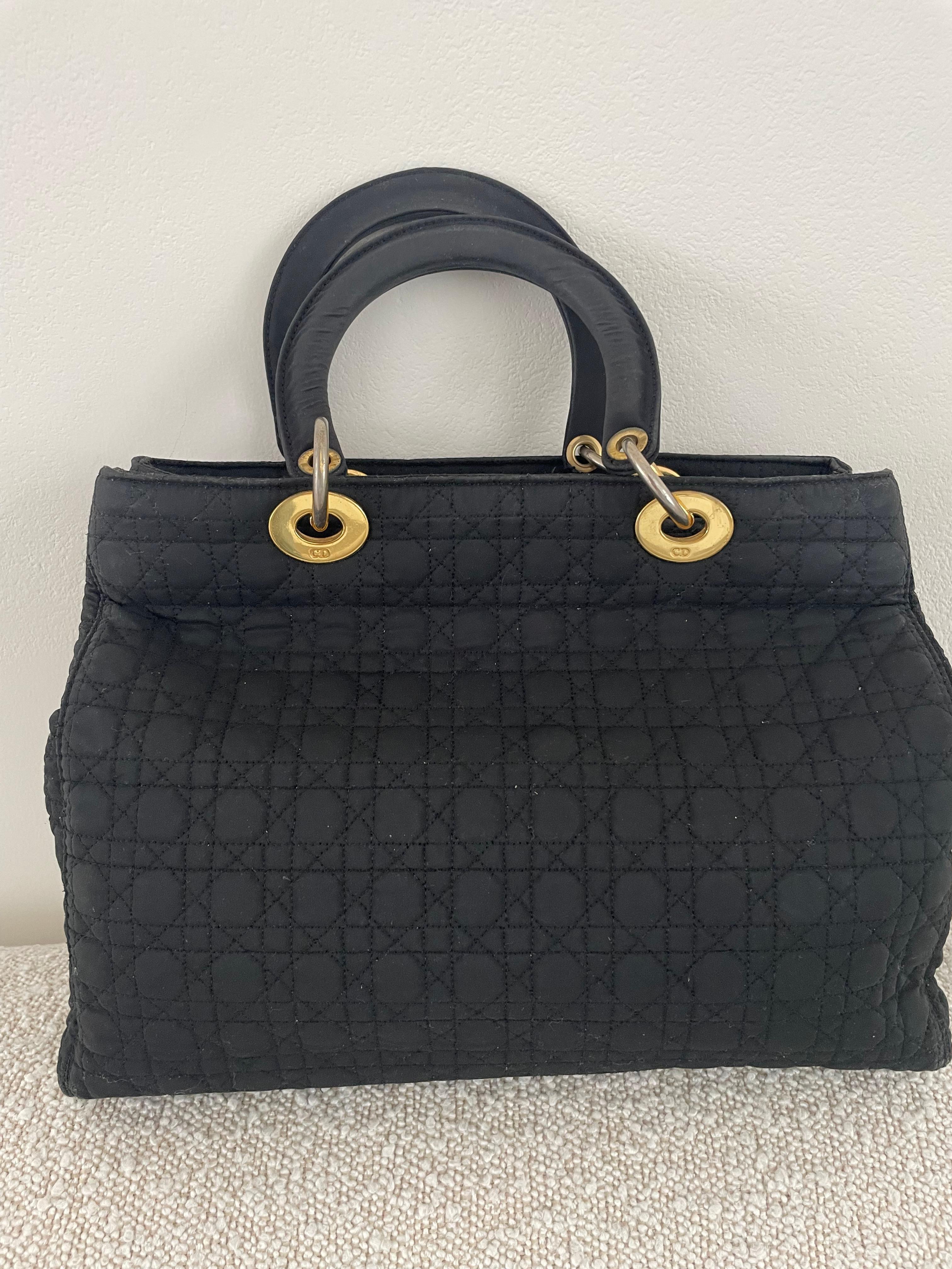 This large authentic Christian Dior Lady Nylon Tote Bag from 1995 is a remarkable piece that embodies the fashion trends of the 1990s, combining practicality with luxury. Its stunning gold-tone hardware, its minimalist design, spaciousness, and