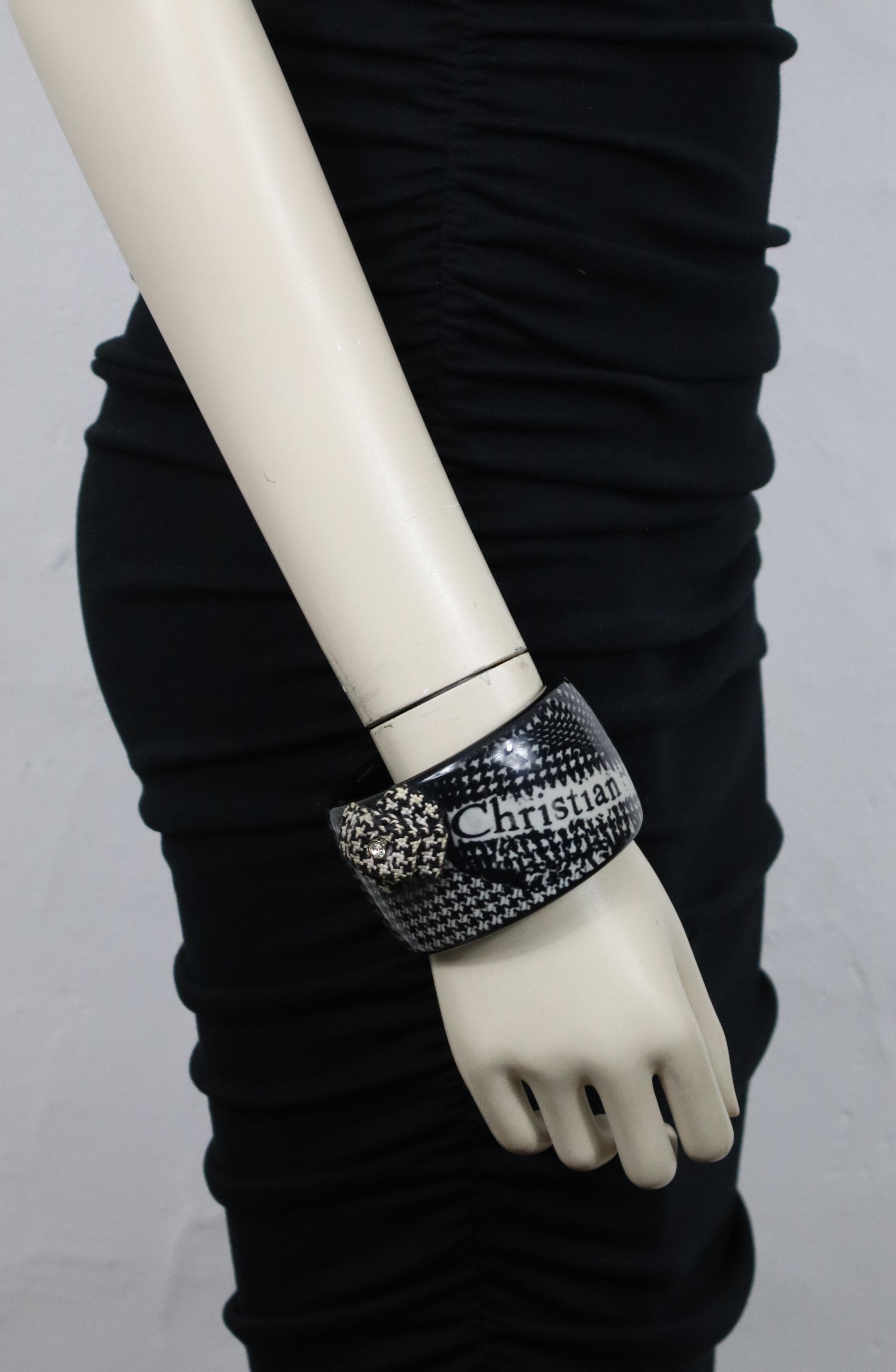 Brazalete CHRISTIAN DIOR de resina blanca y negra con estampado de pata de gallo y logotipo CHRISTIAN DIOR, adornado con una flor de tela y un cristal transparente.

No hay firma en la cara interior.

Medidas orientativas: diámetro total aprox. 8 cm