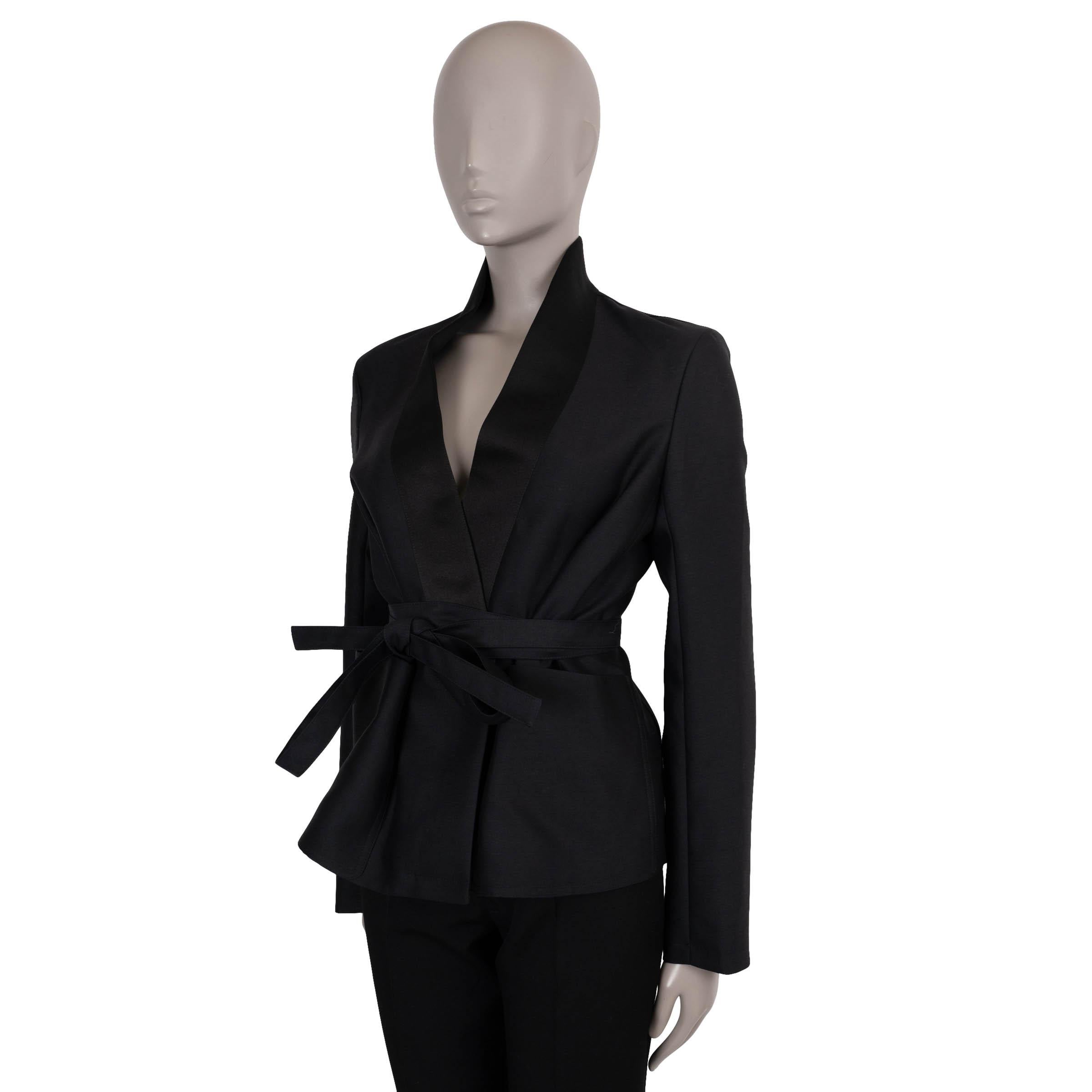 This 100% authentic Christian Dior Palto jacket is crafted in black wool (85%) and silk (15%), combining soft structure with refined elegance. The relaxed silhouette cinches at the waist with a self-tie belt, while the kimono-style collar and two