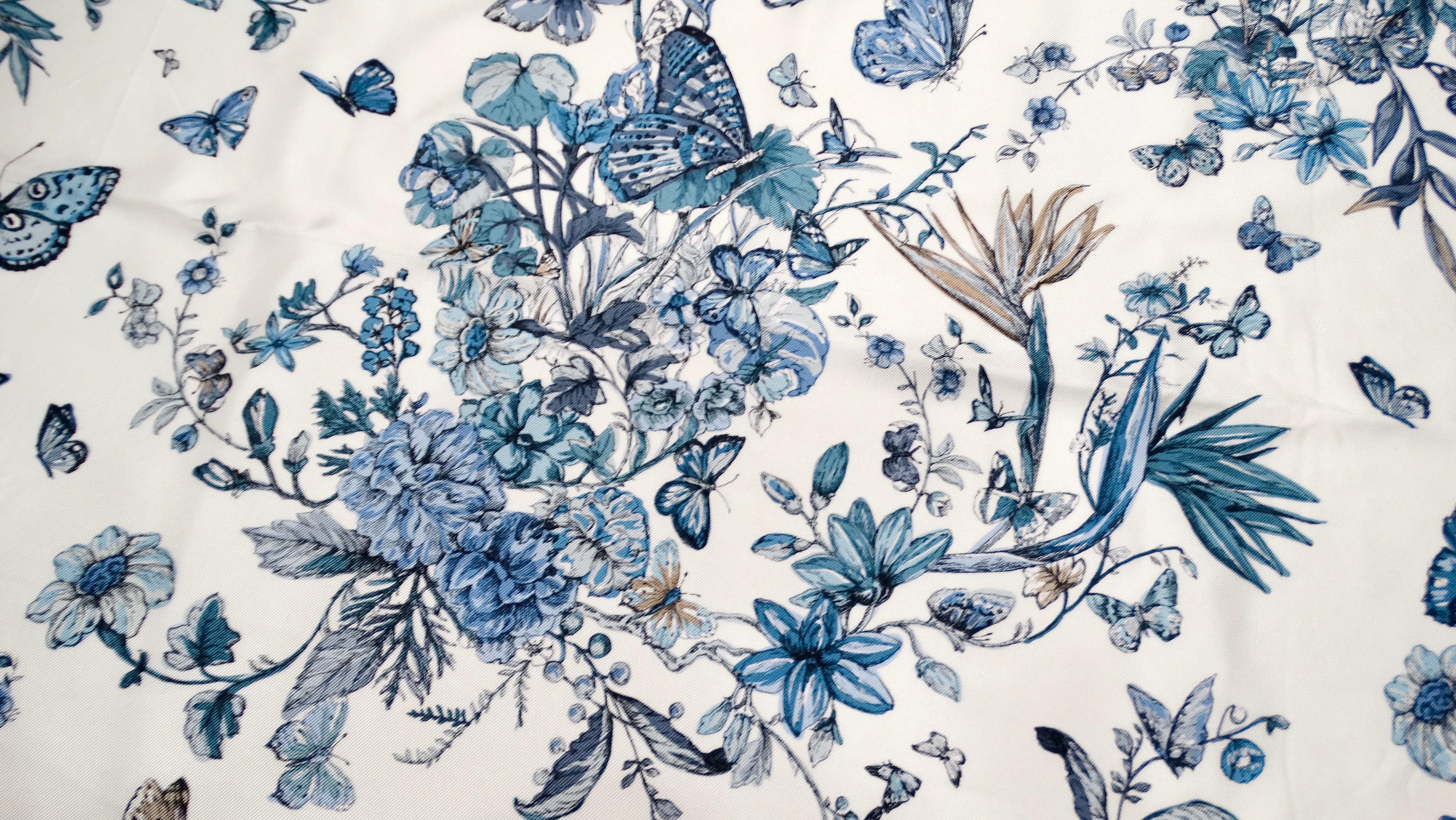 The Christian Dior Blue & White Butterfly Garden Print Silk Scarf embodies a captivating blend of elegance and vibrant artistry, making it a timeless accessory for the modern luxury aficionado. The intricate butterfly garden motif showcases Dior’s