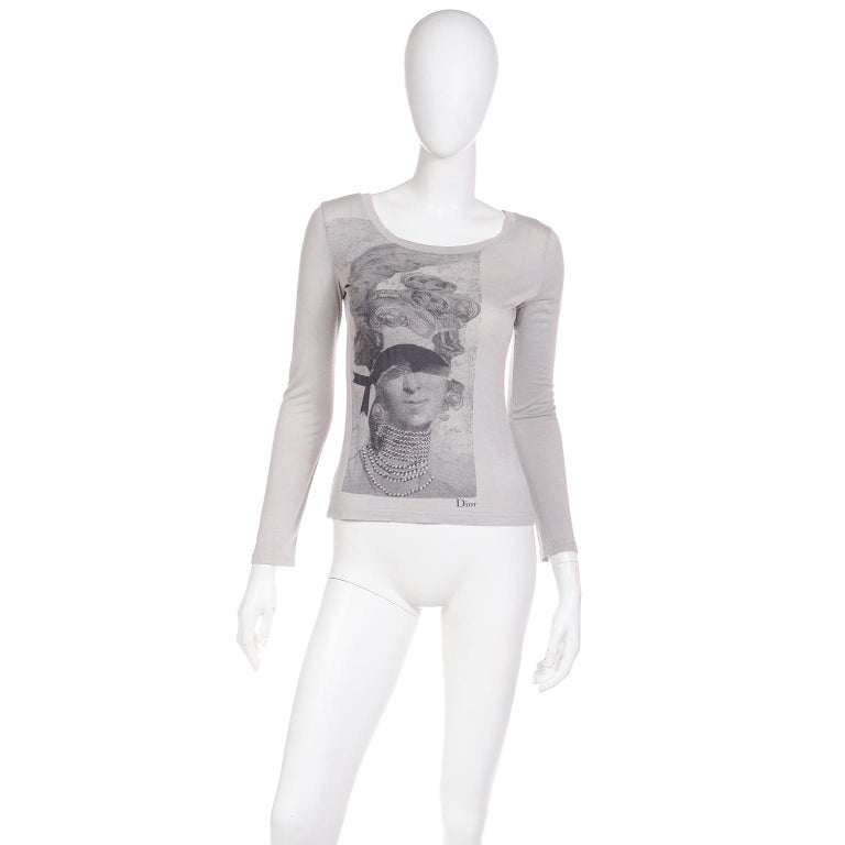 This vintage 2000 Christian Dior John Galliano long sleeve light grey graphic tee shirt features a woman similar to Marie Antoinette (but with a face that looks quite a bit like Galliano) wearing multiple strands of pearls, a feather in her pouf
