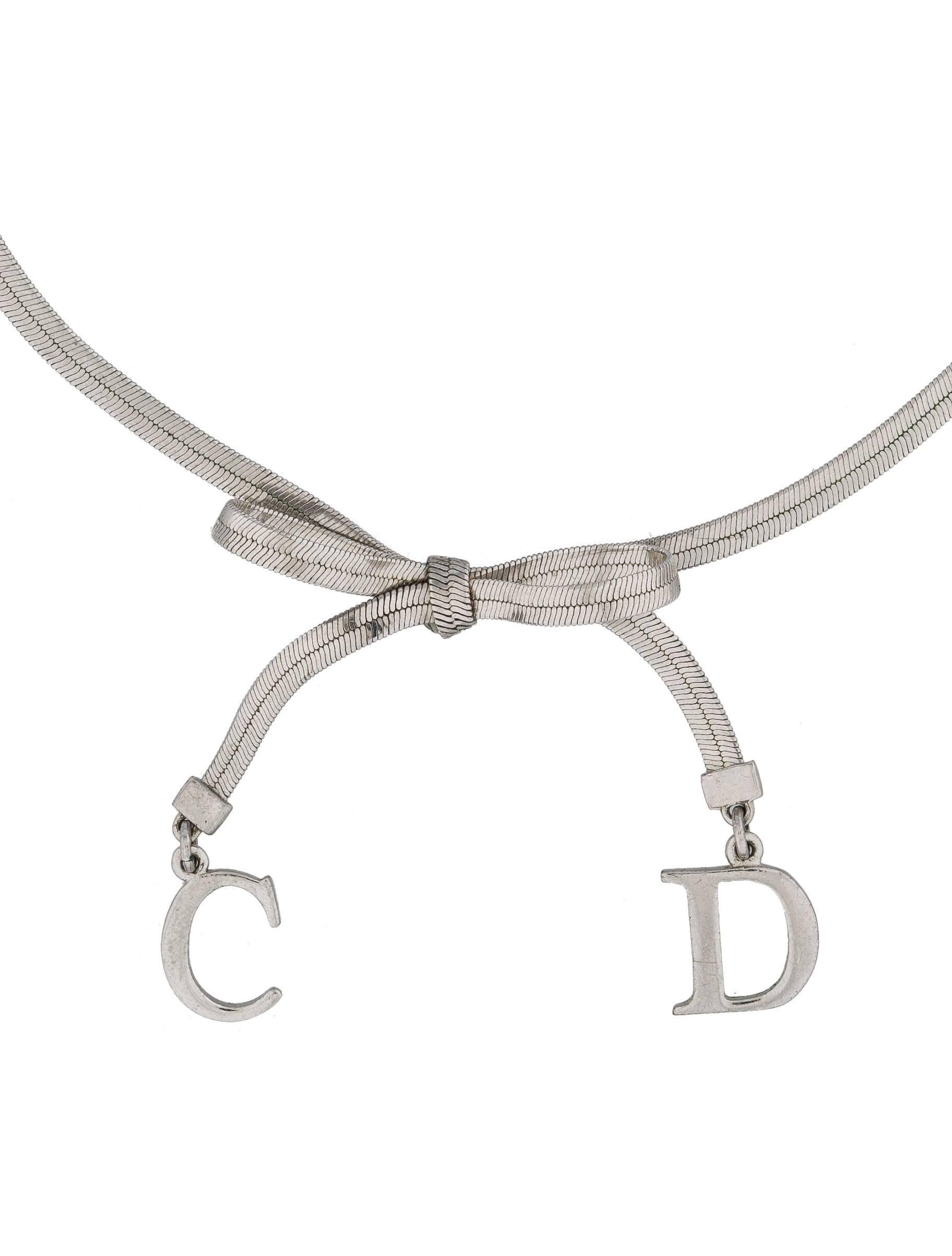 Choker chain necklace by Dior with a bow and CD charms. From John Galliano Era.

Necklace measures 12” to 14”, adjustable, with approximately 1 ½” drop.
Chain is 3 mms wide. Color is silver.