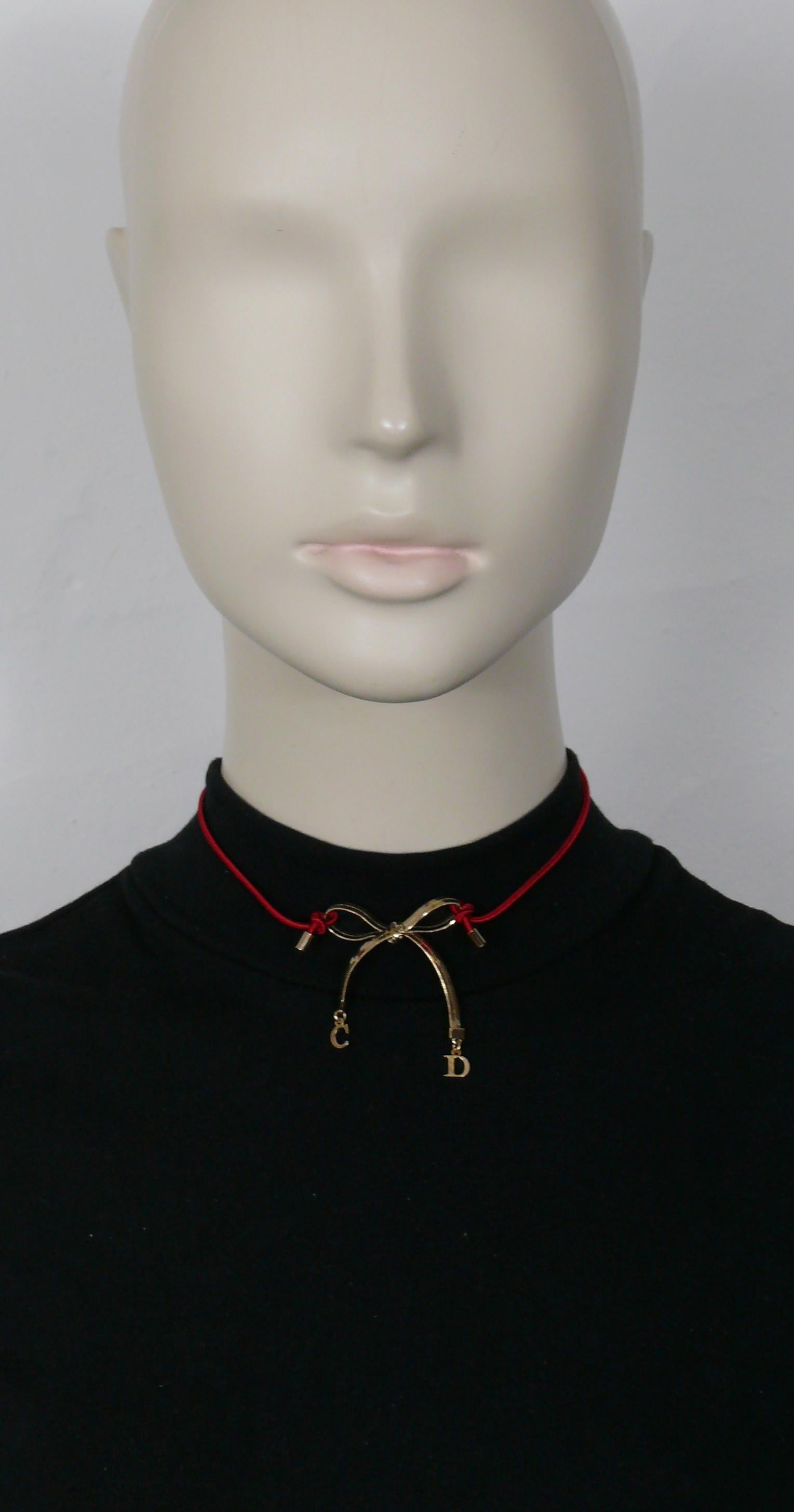 Collier ras-de-cou CHRISTIAN DIOR avec nœud en métal doré et breloques initiales C.I.D., sangle rouge élastiquée.

Fermeture avec un fermoir en forme de homard.
Longueur réglable.

Embossé DIOR.

Mesures indicatives : longueur réglable d'environ 33