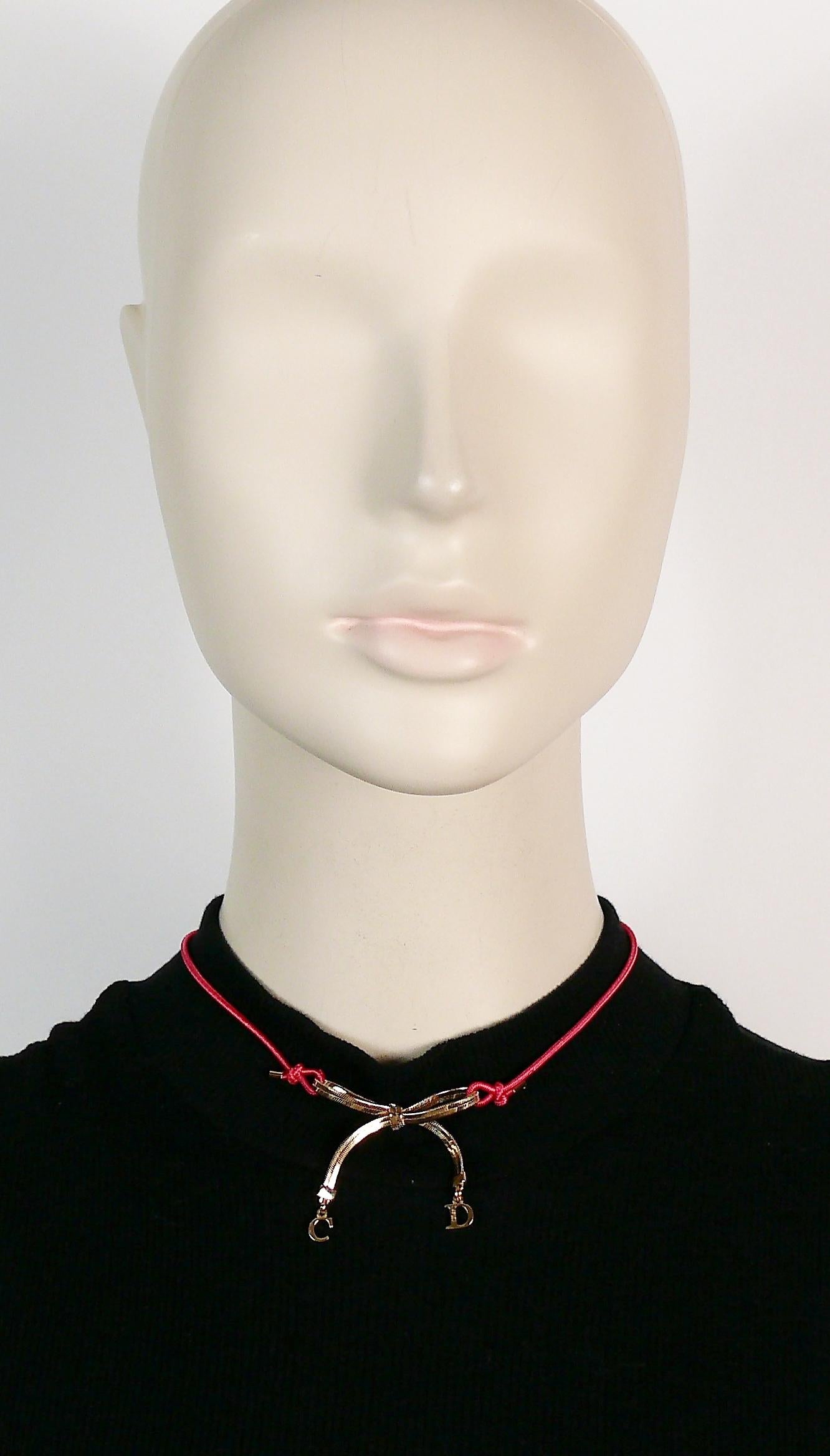 CHRISTIAN DIOR choker necklace featuring gold toned bow and CD charms, red elasticated strap.

Lobster clasp closure.
Adjustable length.

Embossed DIOR.

NOTES
- This is a preloved vintage item, therefore it might have imperfections.
- Colors may