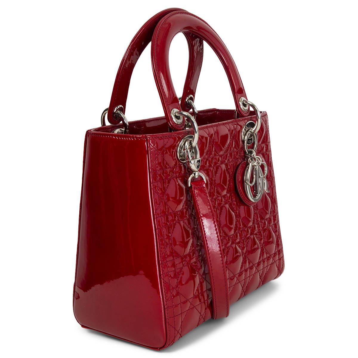 100% authentic Christian Dior Medium Lady Dior bag is crafted in burgundy red patent calfskin with signature Cannage stitching. Silver-finish metal hardware and the 'D.I.O.R.' charms complete and illuminate its silhouette. Featuring a thin,