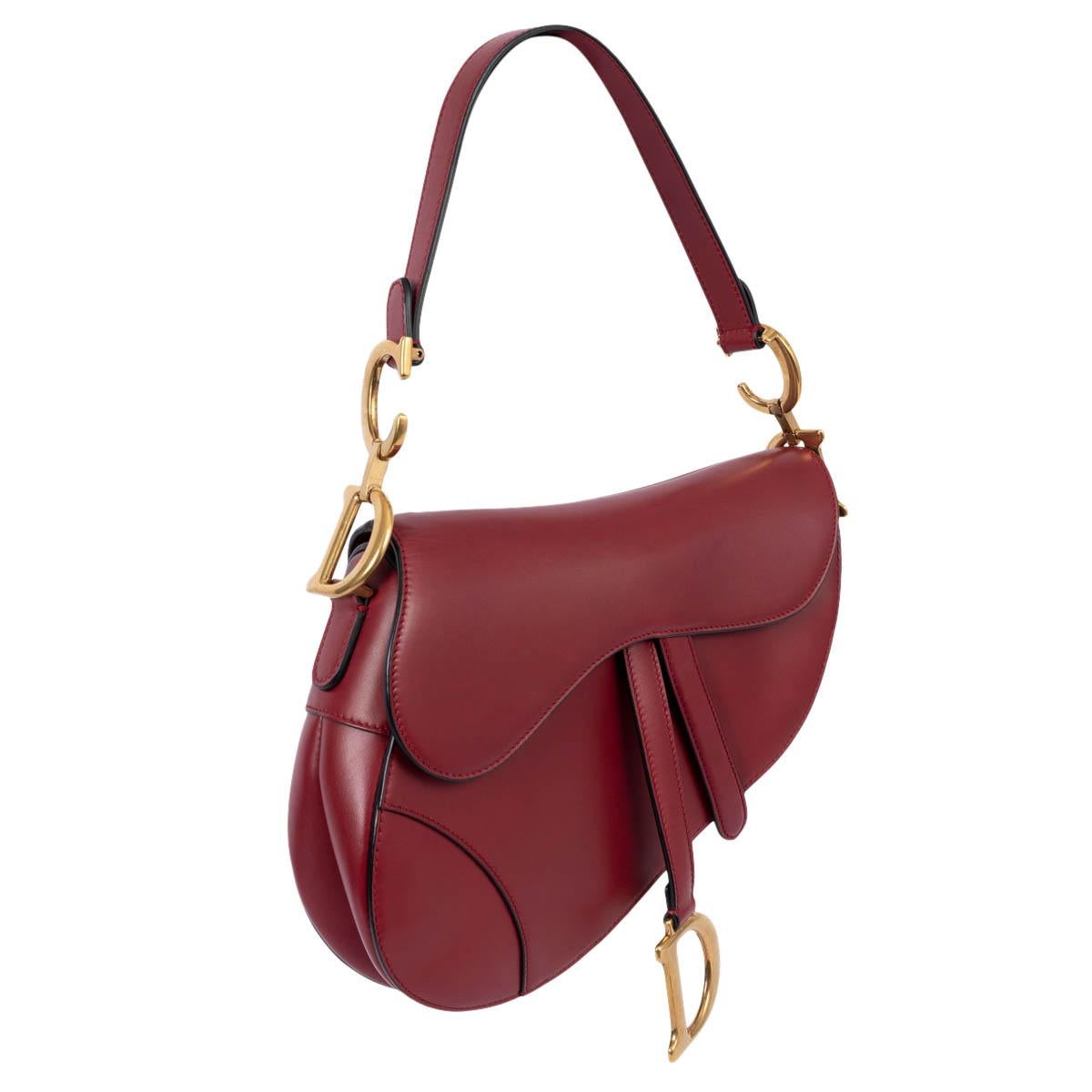 100% authentic Christian Dior Saddle bag in burgundy smooth calfskin. The legendary design features a Saddle flap with a D stirrup strap and magnetic pull, as well as an antique gold-finish metal CD signature on either side of the handle. The design