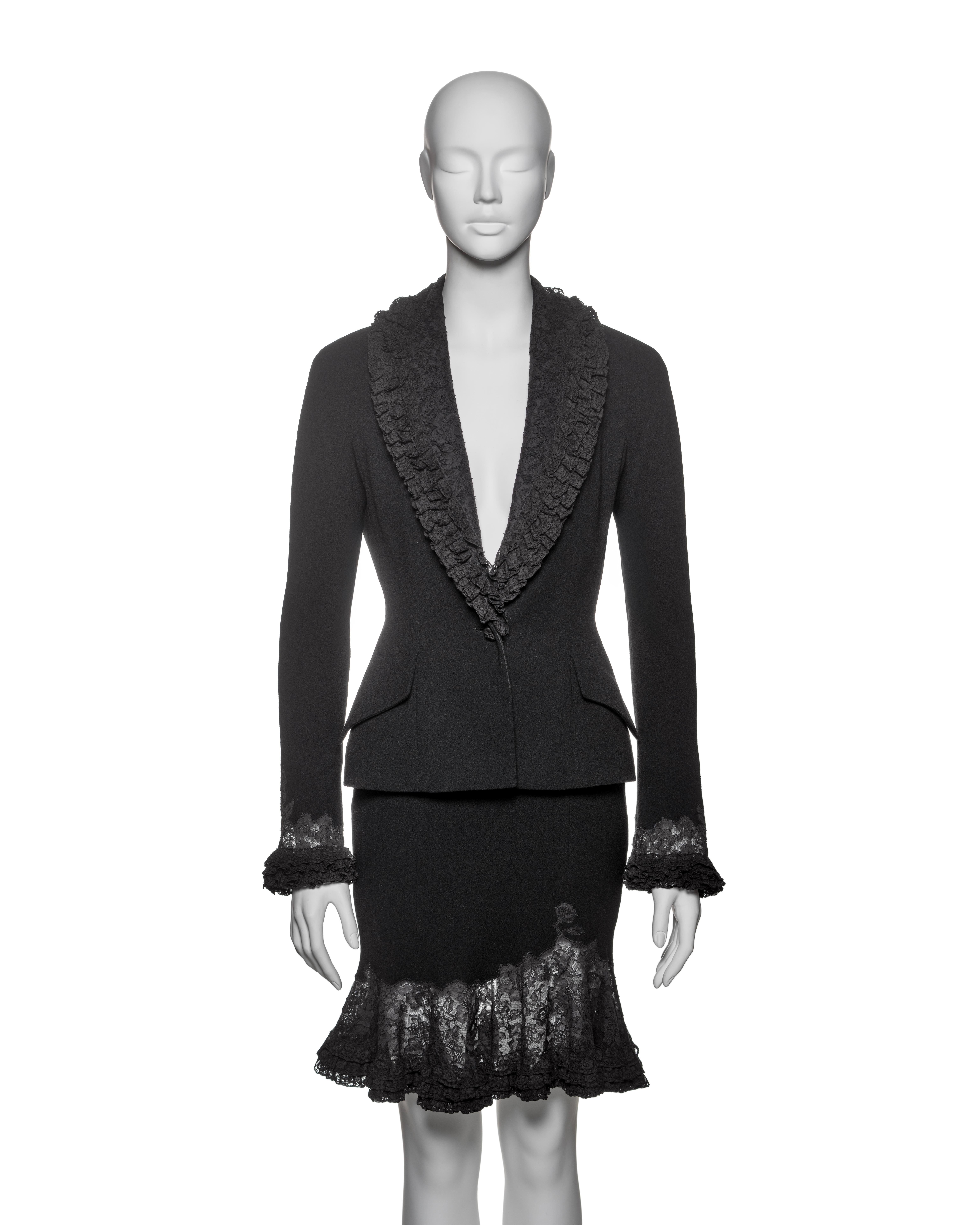This Christian Dior by John Galliano suit from the Fall-Winter 1998 collection is constructed from black crepe and features intricate lace details. The jacket showcases a tailored silhouette with a single-button closure, peak lapels adorned with