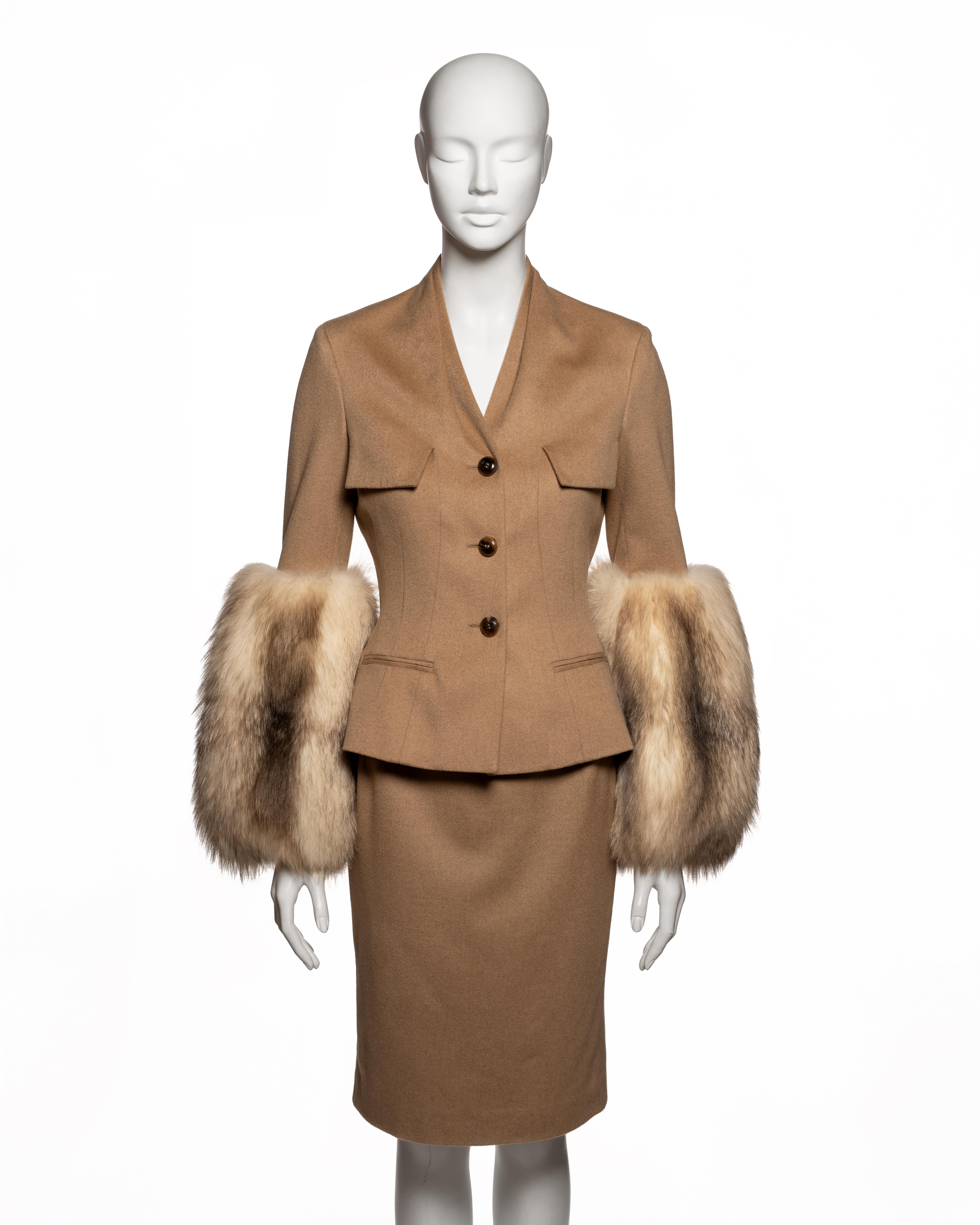 Abito con gonna sartoriale di John Galliano for Christian Dior della collezione Autunno-Inverno 2007, realizzato in cammello con fodera in seta jacquard tono su tono. La giacca, dal taglio deciso, presenta una profonda scollatura a V, una linea di