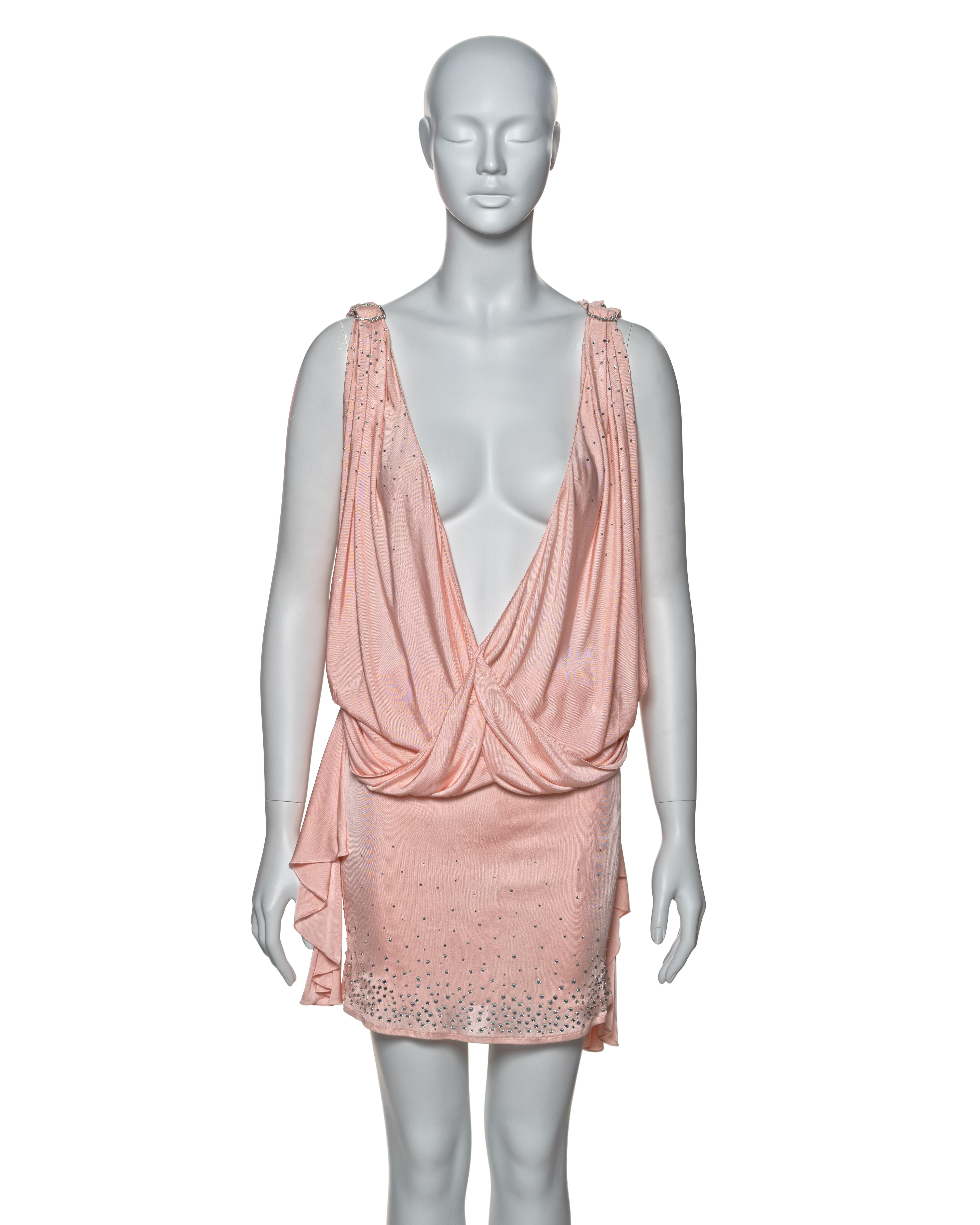 This Christian Dior dress, crafted in bias-cut pink silk jersey, features a mini-length design with a plunging cowl neckline. The shoulders and sides are adorned with crystal-encrusted buckles, leading to cascading drapes that enhance the fluid