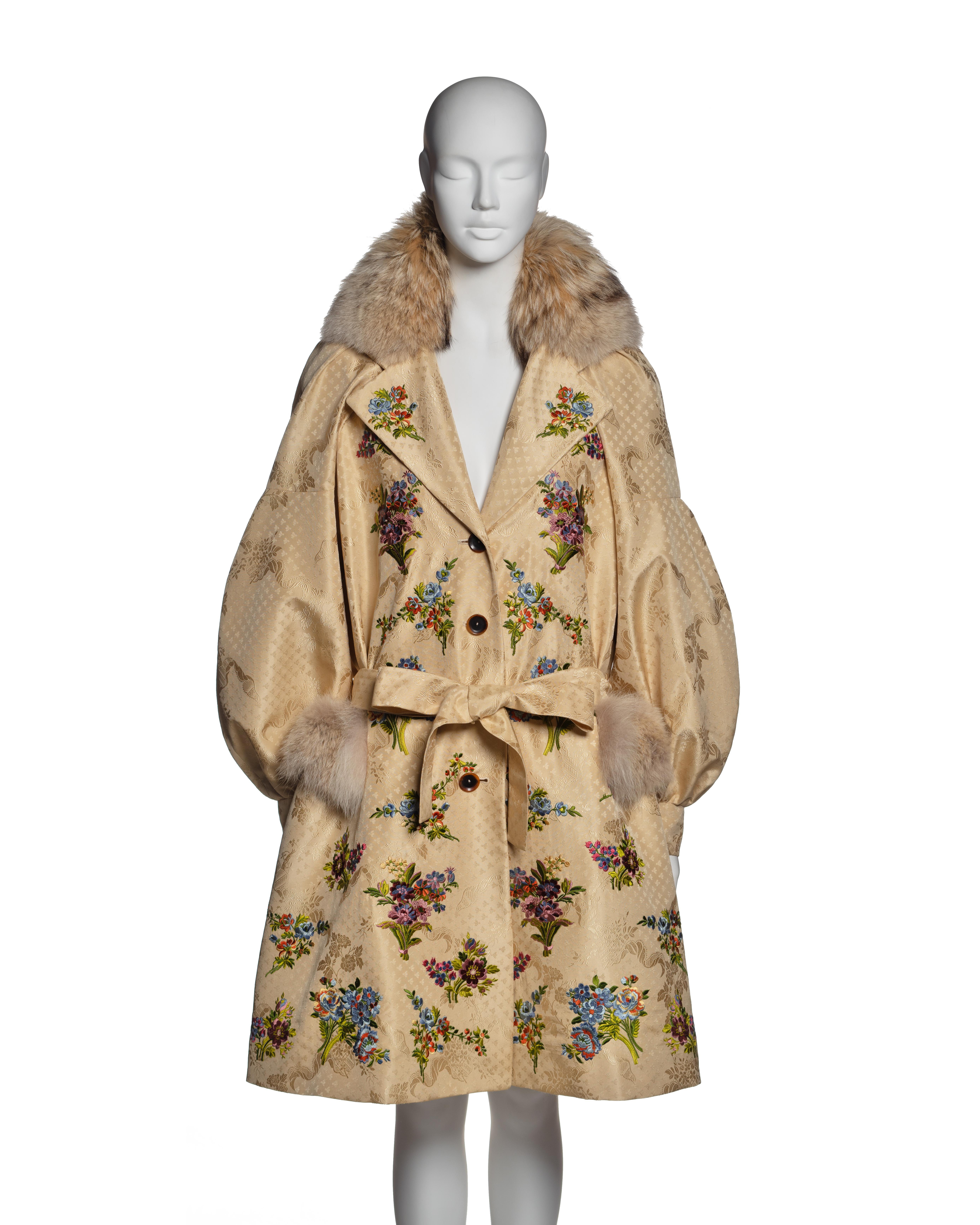 This Christian Dior by John Galliano coat from the Fall-Winter 2002 collection is crafted from cream silk jacquard featuring an elaborate woven pattern of floral and ornamental motifs. The coat is adorned with multicolored floral embroidery in