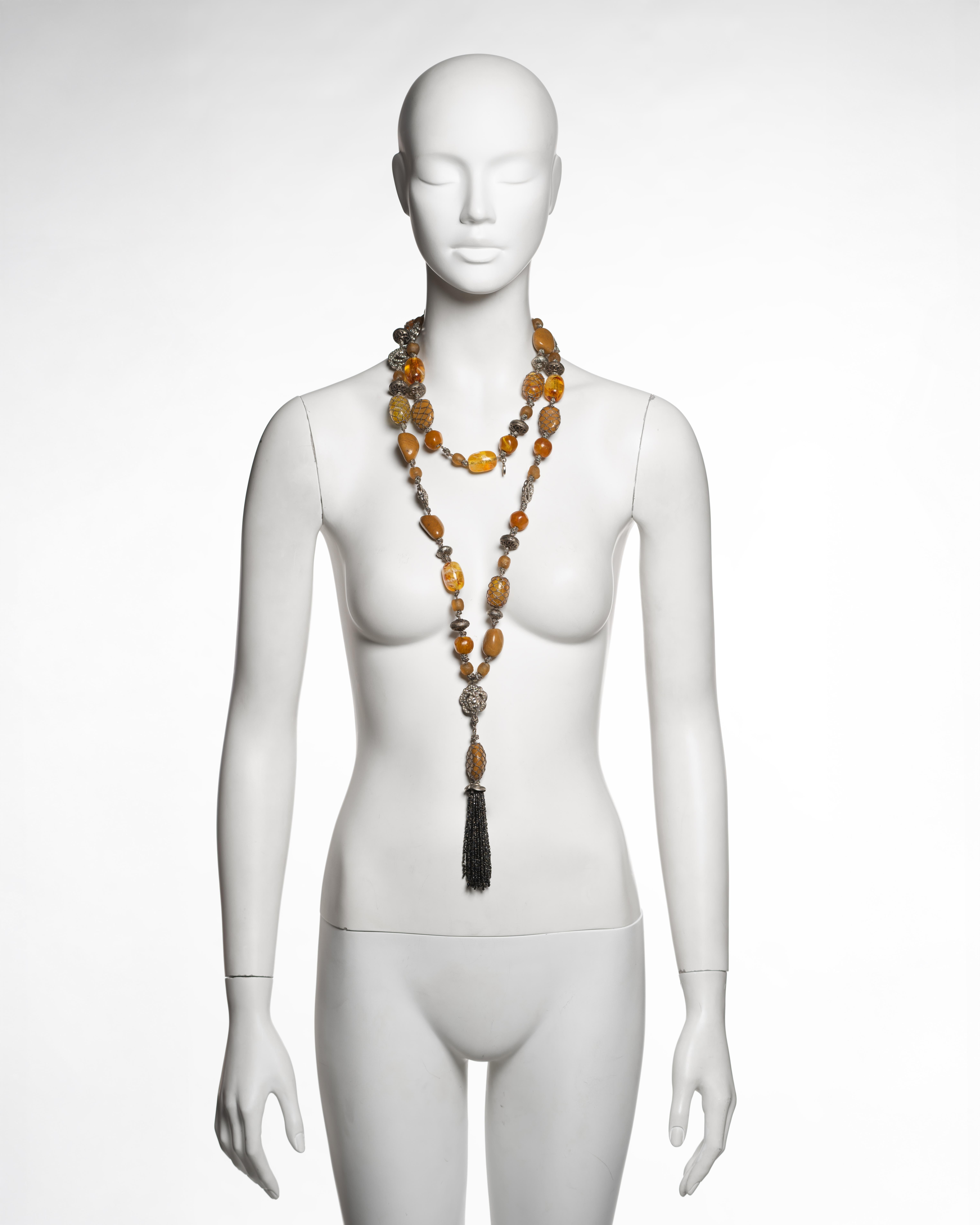 Long necklace by Christian Dior under the direction of John Galliano, produced in 1998. The piece is composed of irregular amber resin beads in tones ranging from honey to ochre, interspersed with matte and polished metal spacers and ornamental