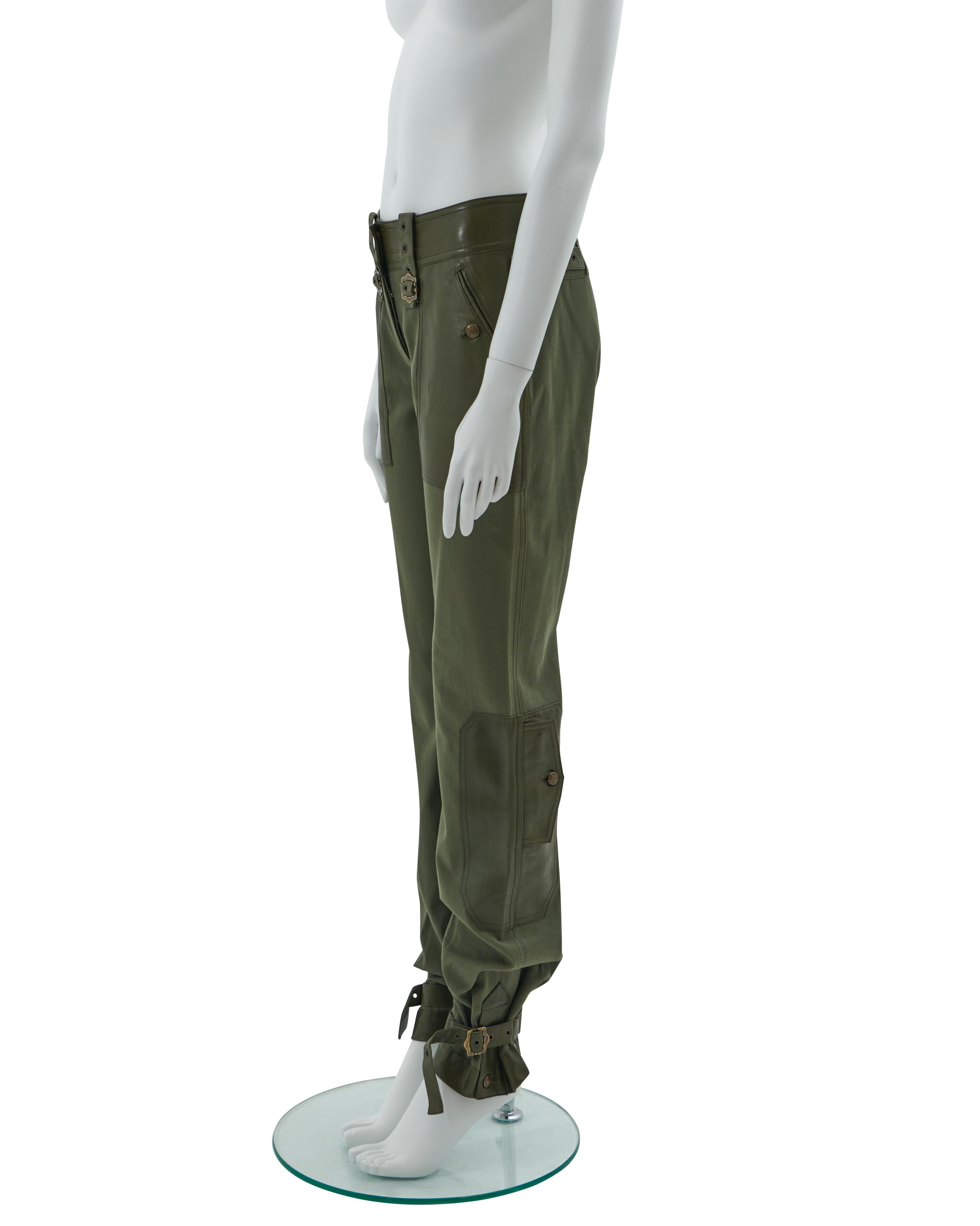 - Designed by John Galliano
- Sold by Skof.Archive
- Khaki olive green cotton canvas and leather cargo pants
- Leg embellished with pin buckles in coordinated leather and aged gold-tone metal
- Adjustable buckles on the button
- Two frontal leather